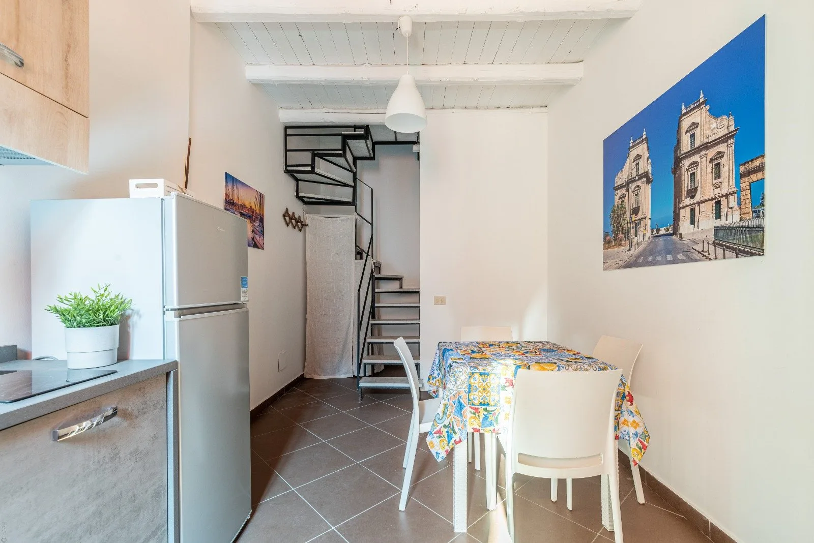 A bright dining area with a table, refrigerator, and staircase.