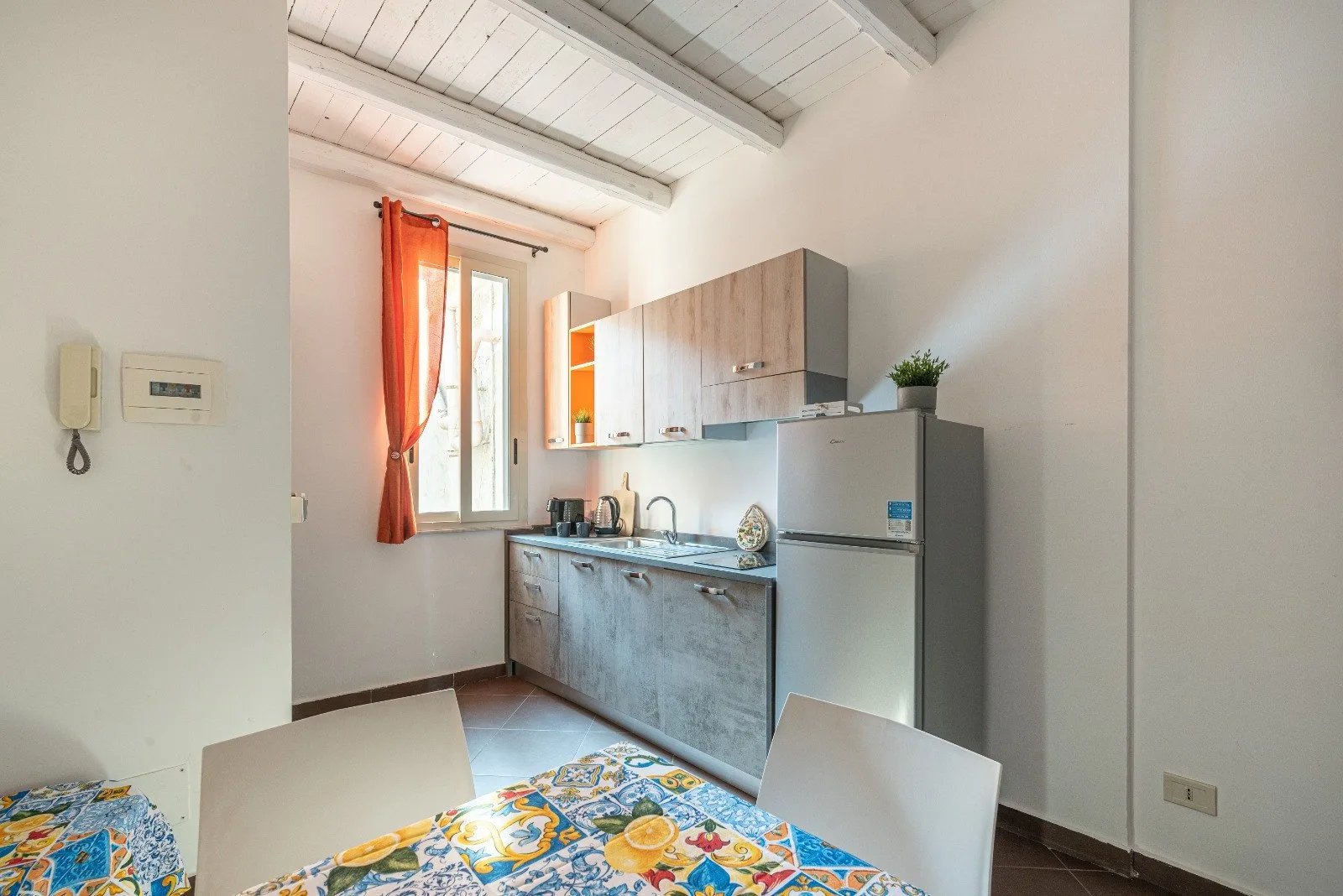 A bright kitchen and dining area with cabinets, a refrigerator, and a patterned tablecloth.