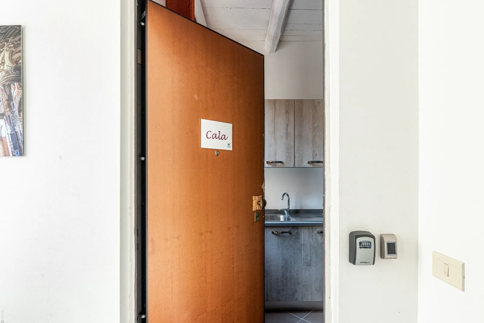 An open wooden door reveals a small kitchen with cabinets and a sink.