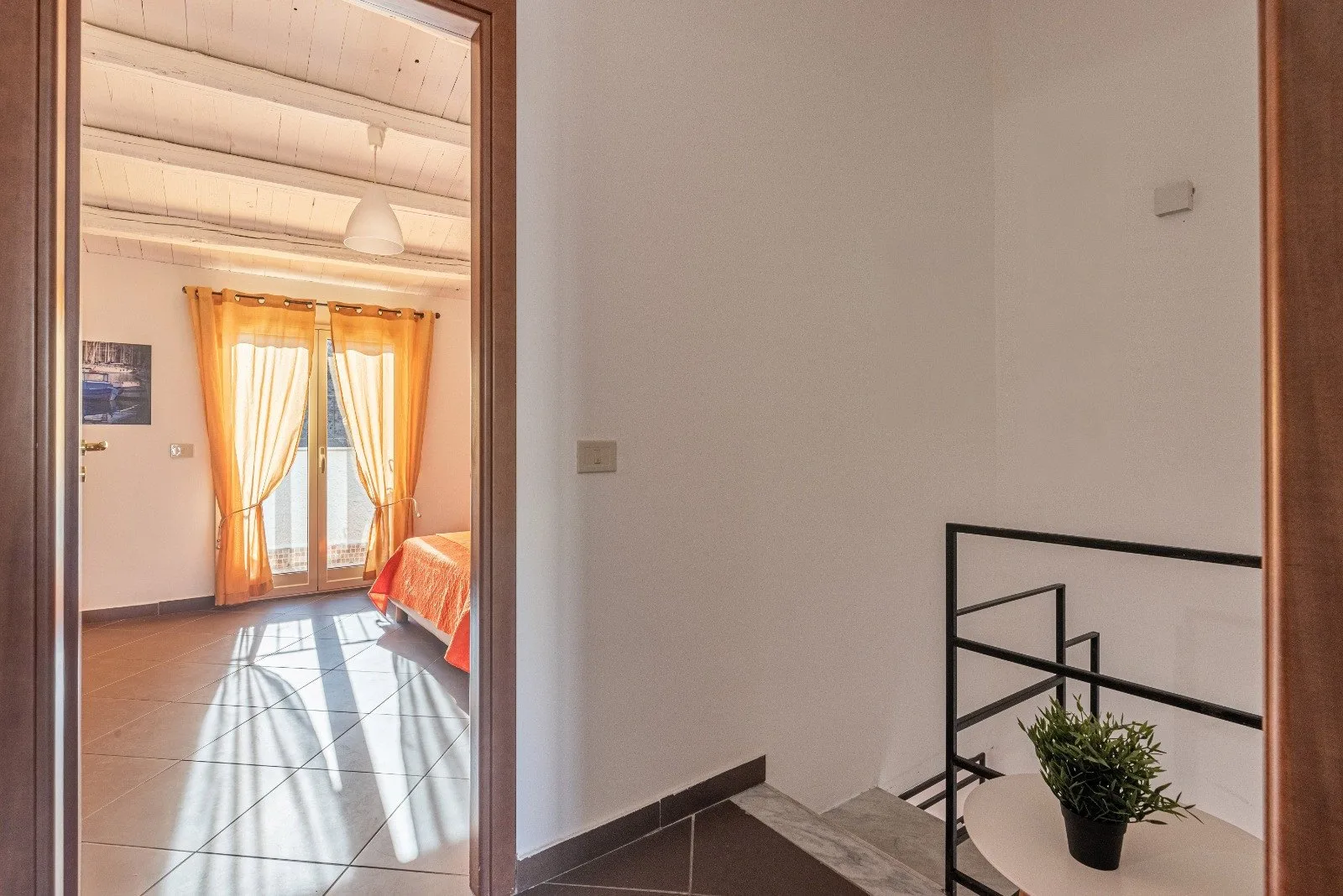 A bright bedroom with orange curtains and sunlight streaming across the tiled floor.