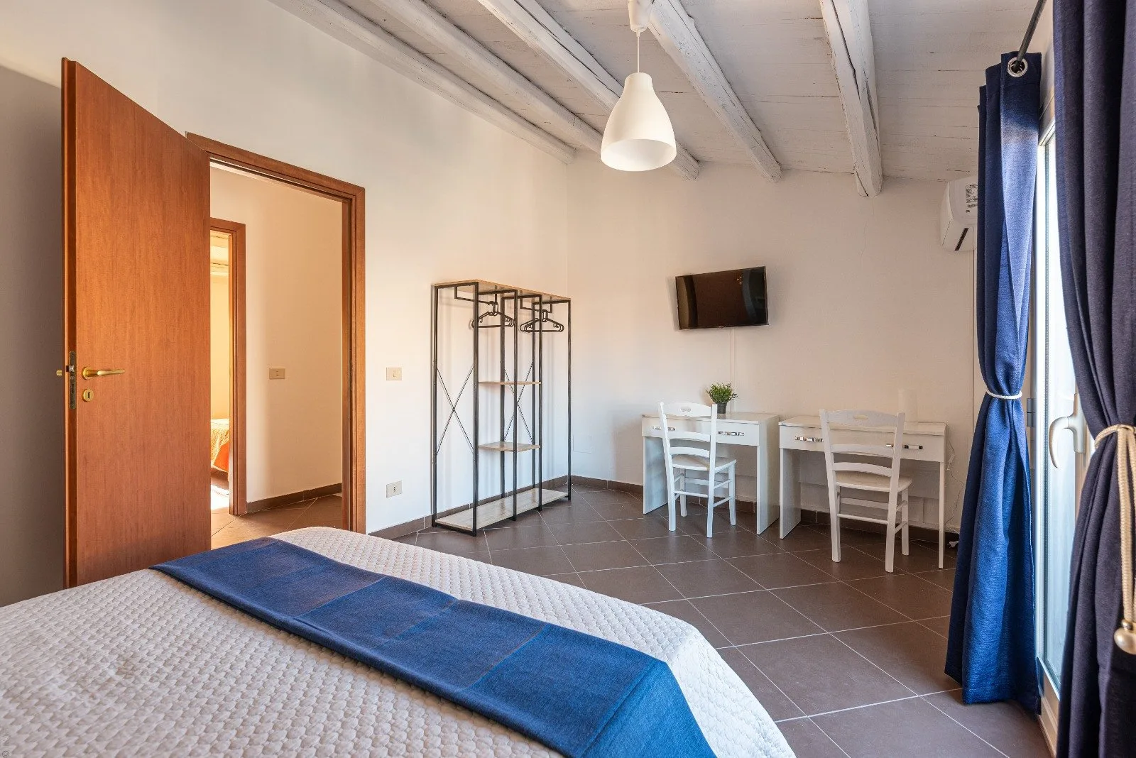 A bedroom with a bed, a small dining table, and blue curtains.