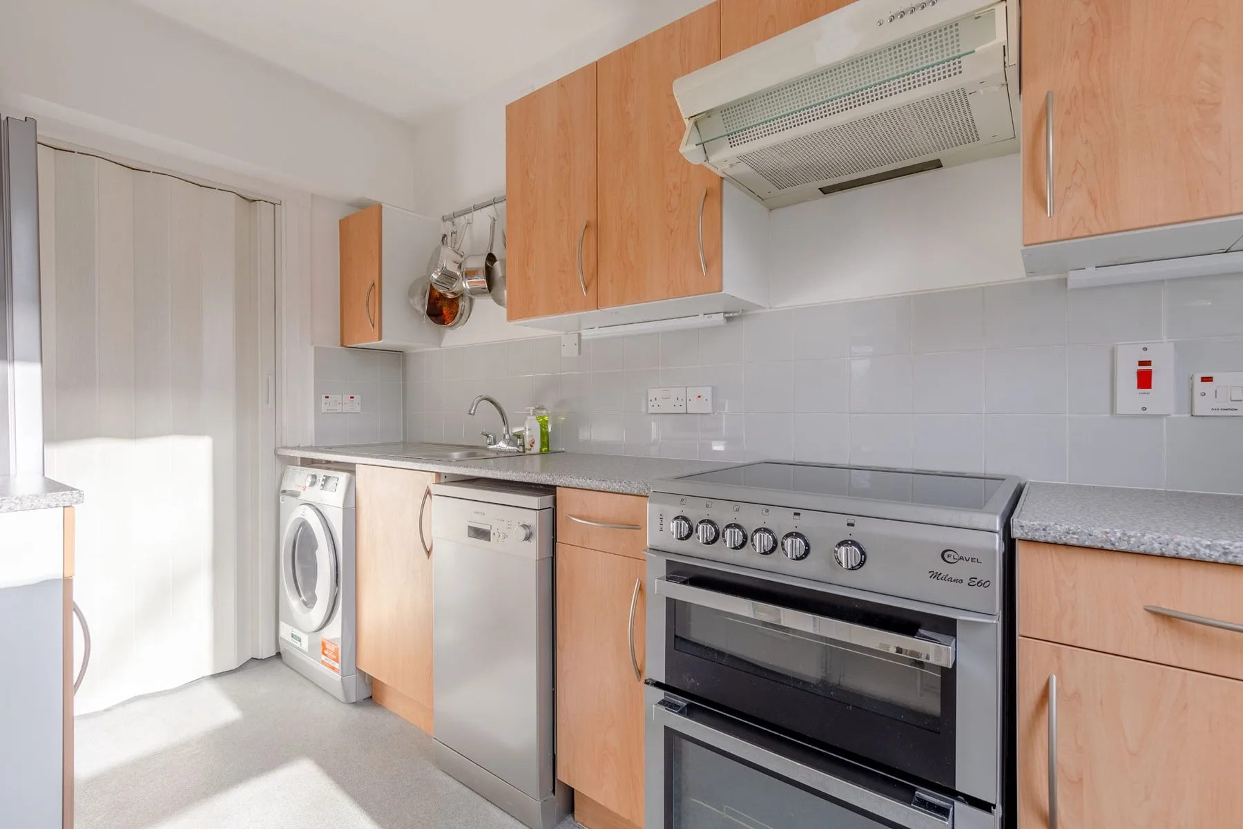 Una cocina con gabinetes de tonos madera, una estufa y electrodomésticos de lavandería.
