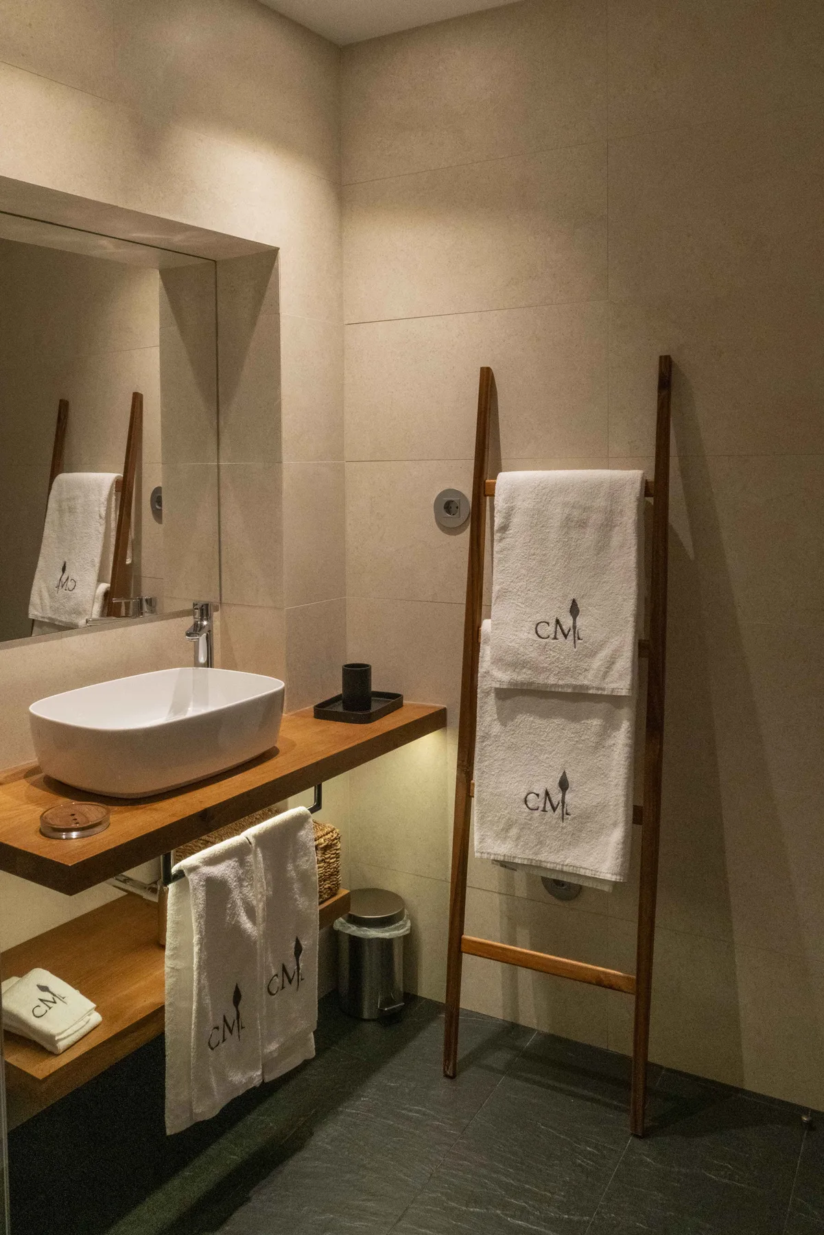 Un lavabo de baño con un lavamanos sobre encimera y toallas en un soporte de madera.