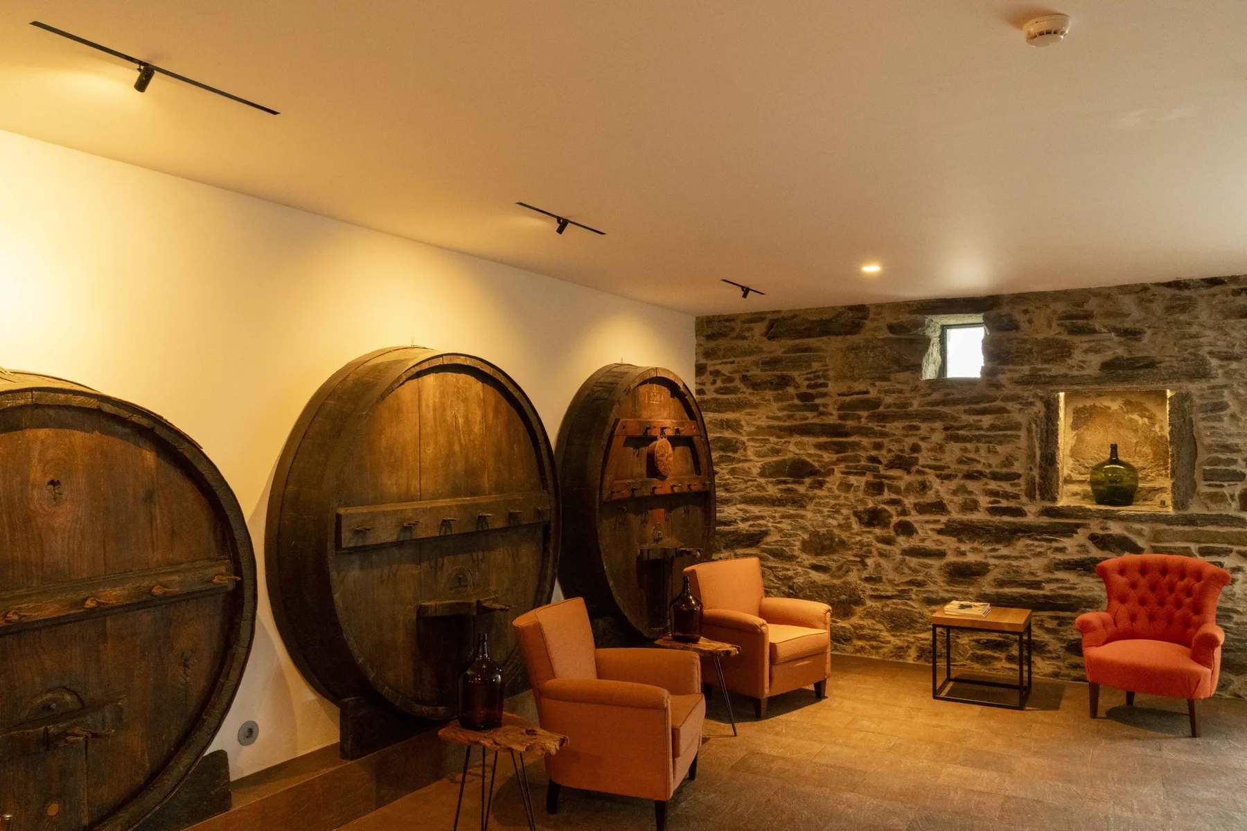 Una sala cálidamente iluminada con grandes barriles de madera y varios sillones.