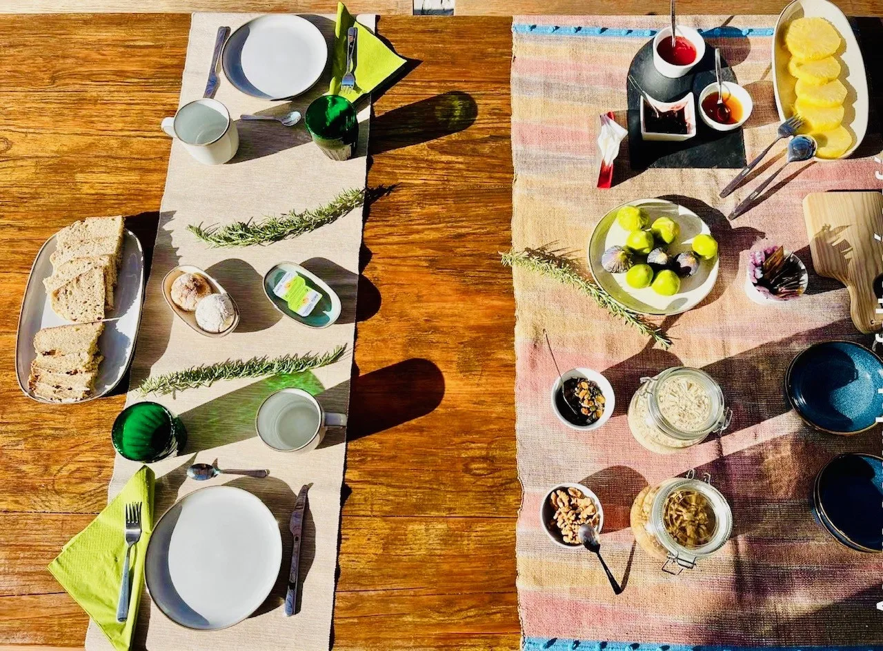 Una mesa está preparada con platos, cuencos, fruta y pan.