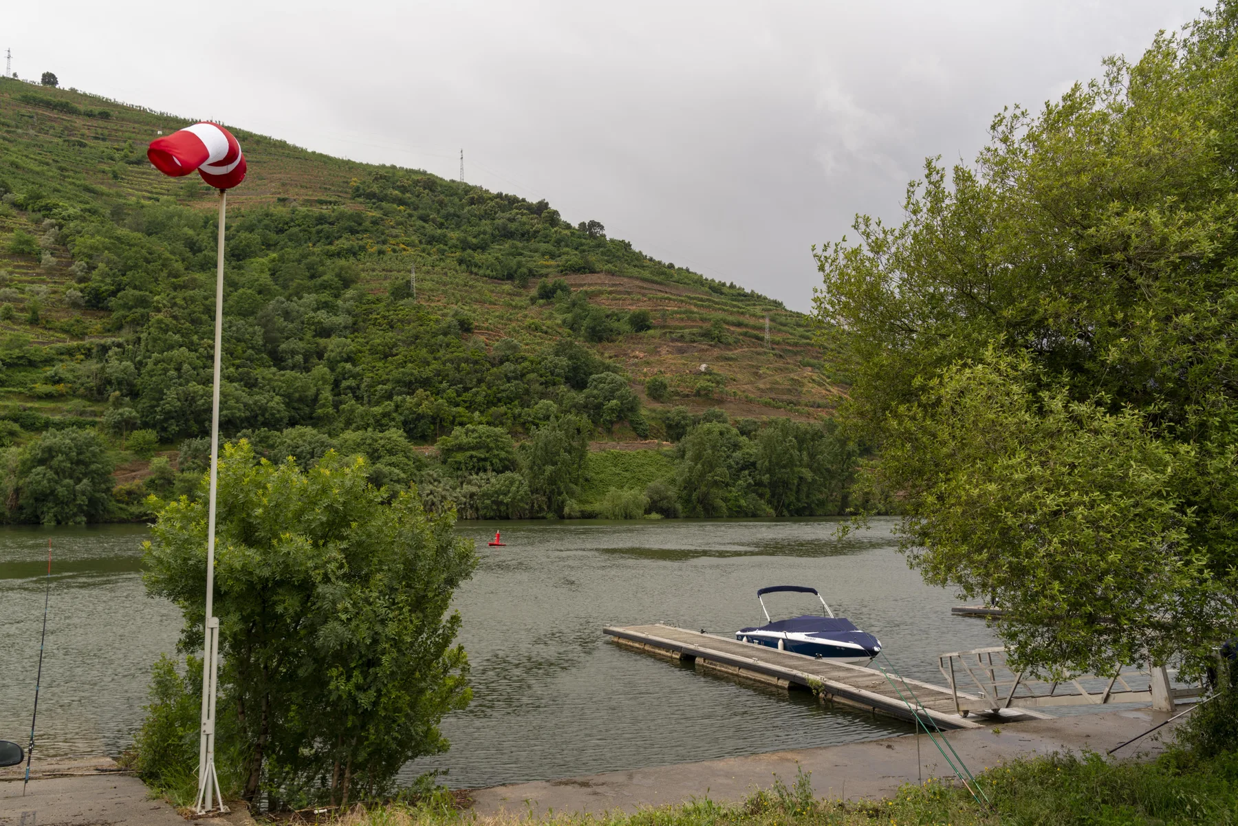 Un embarcadero junto al río con una pequeña embarcación se encuentra al pie de una colina verde.
