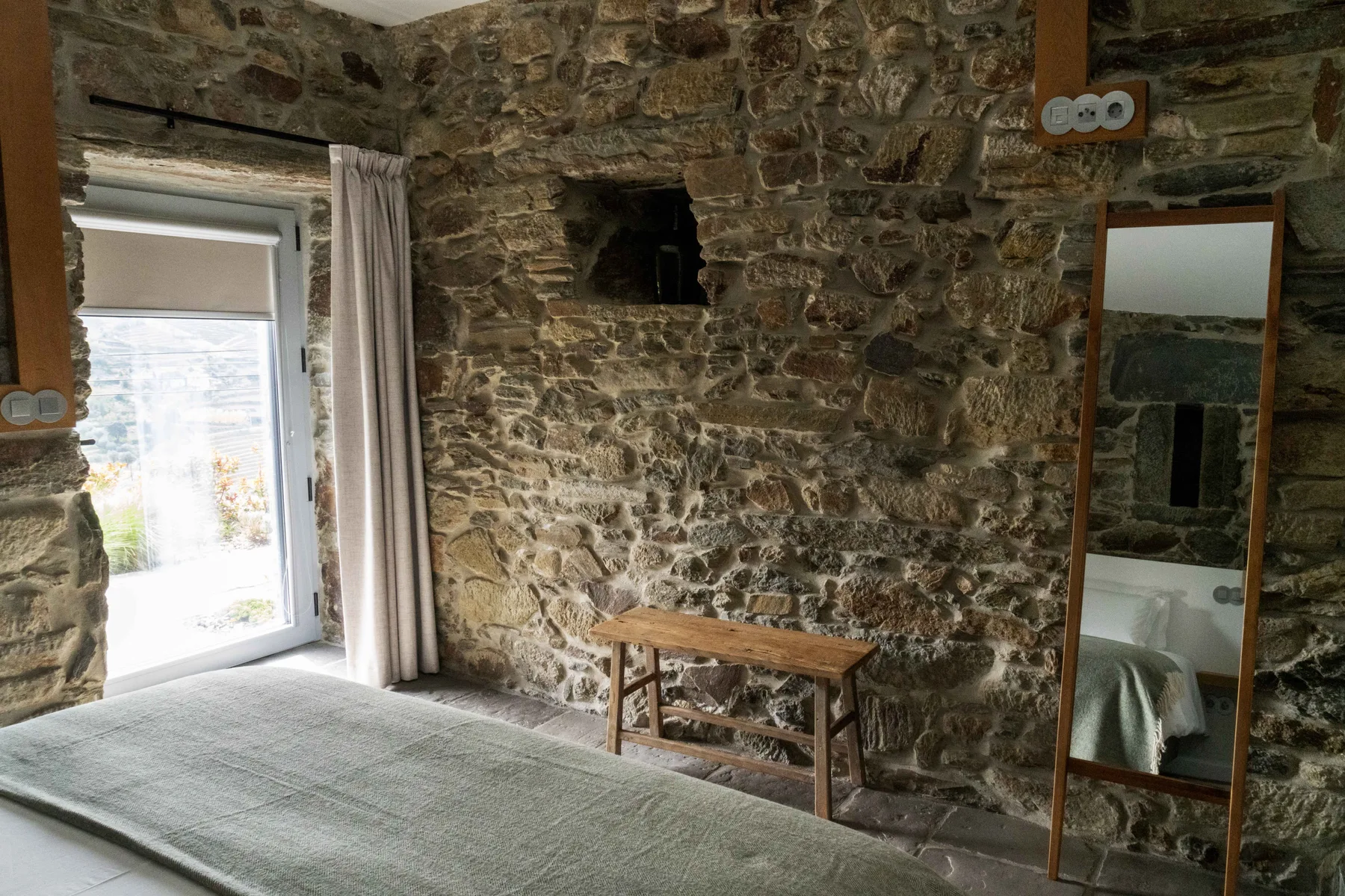 Un dormitorio con paredes de piedra, una cama y una pequeña mesa de madera.