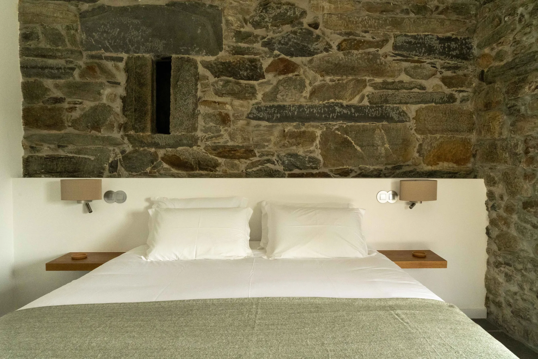 Un dormitorio con una cama bien tendida frente a una pared de piedra rústica.