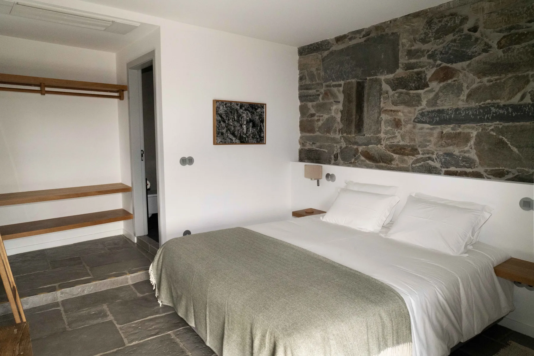 Un dormitorio con ropa de cama blanca junto a un perchero abierto de madera.