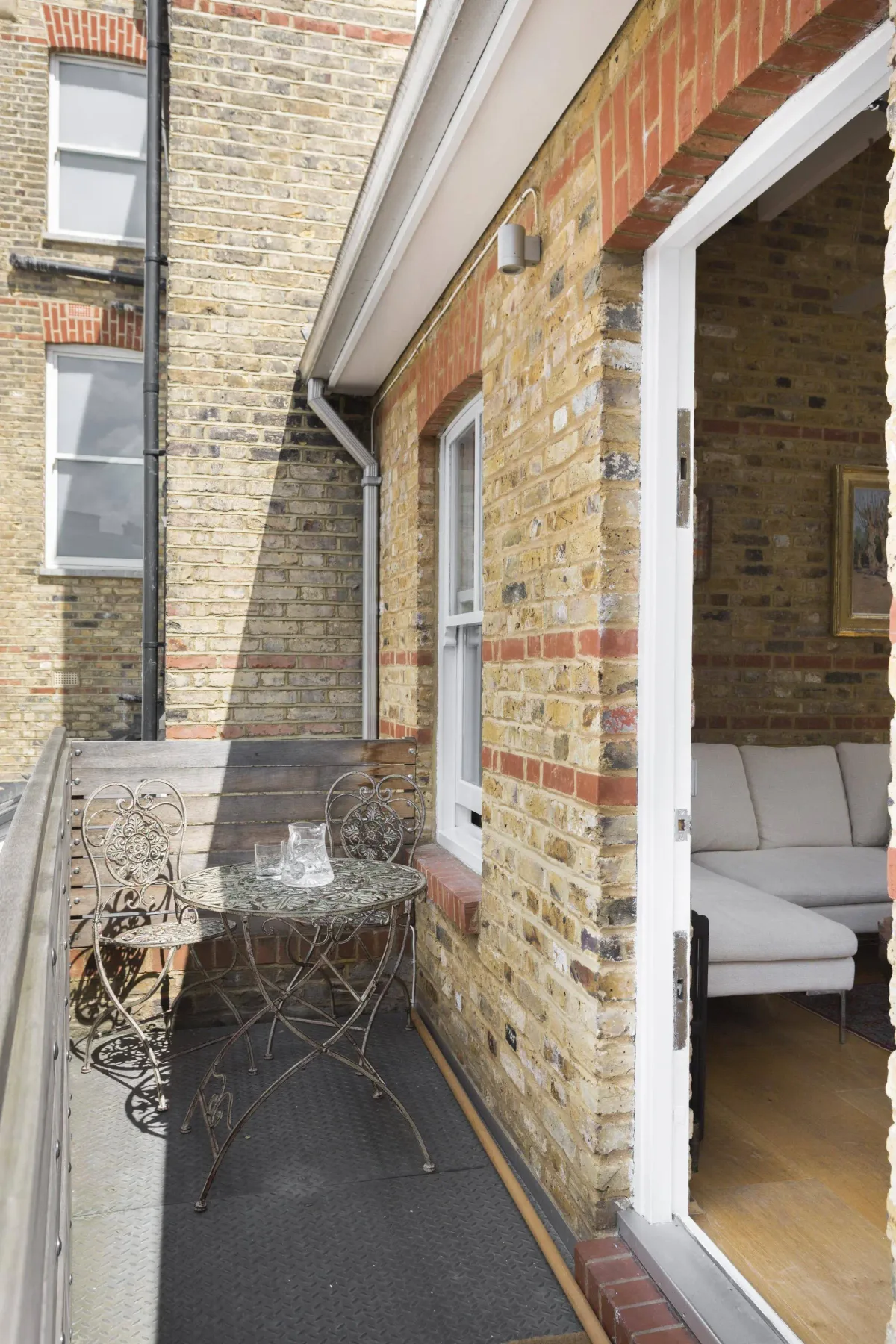 A small brick patio with metal seating sits beside an open doorway.