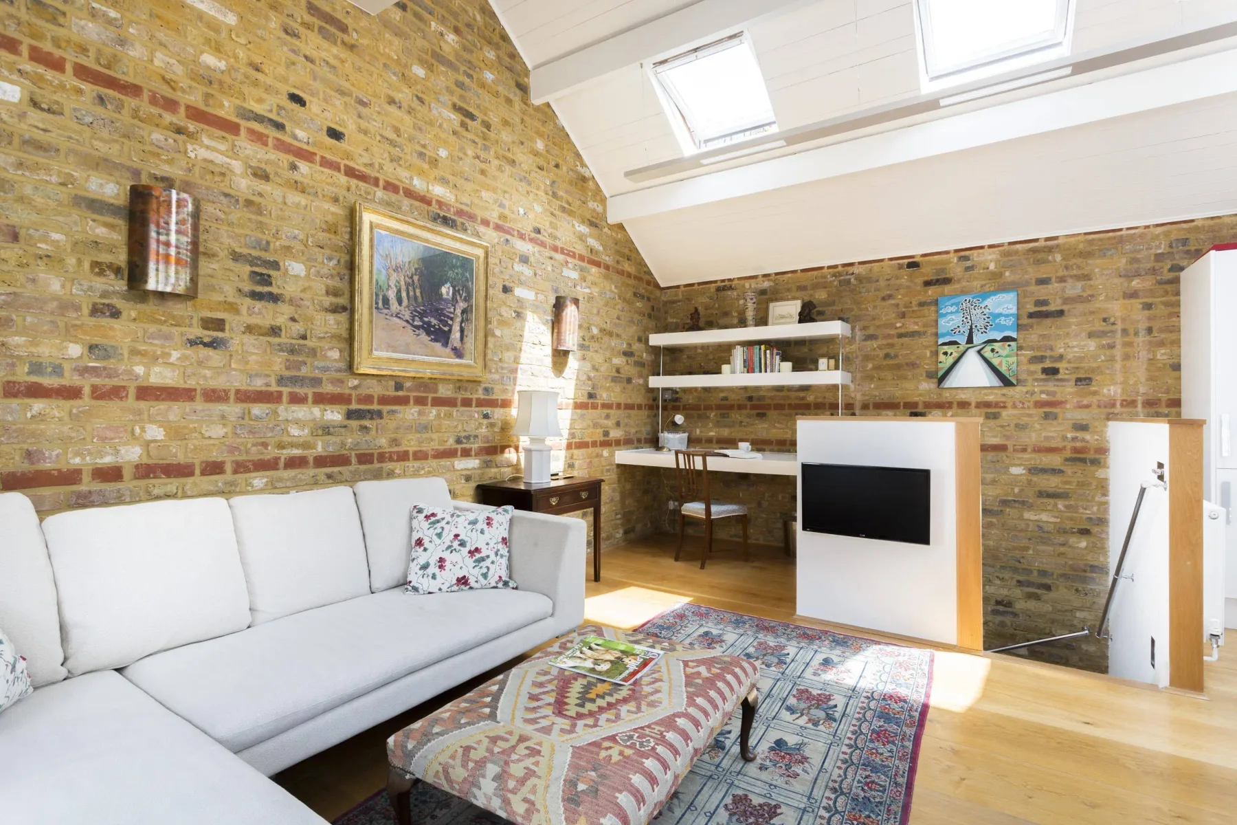 A bright living room with seating, a patterned rug, and exposed brick walls.