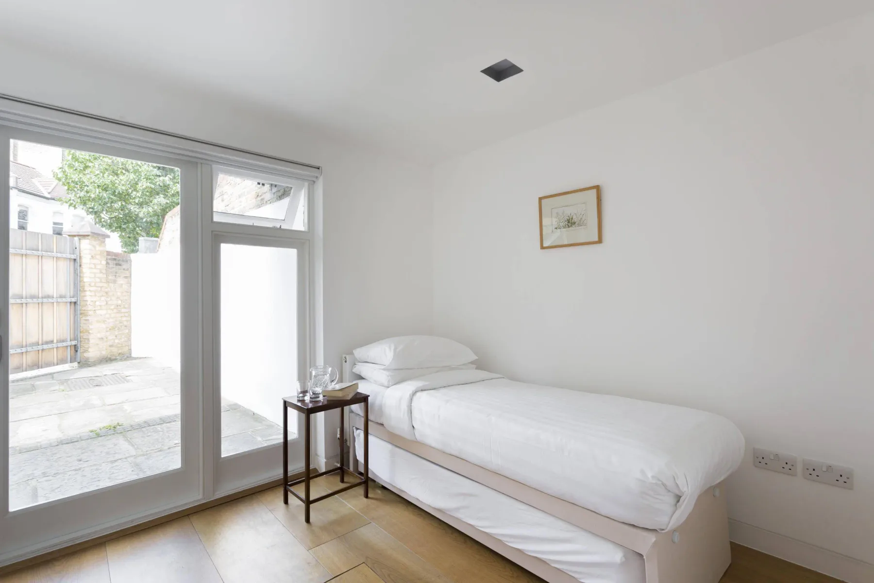 A bright bedroom with a white bed beside large glass doors.