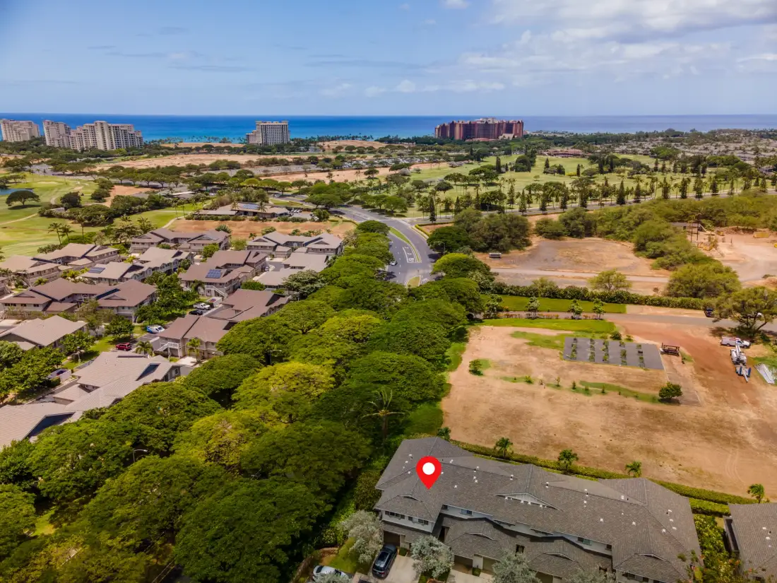 An aerial view of a low-rise building among trees, with the ocean visible in the distance.