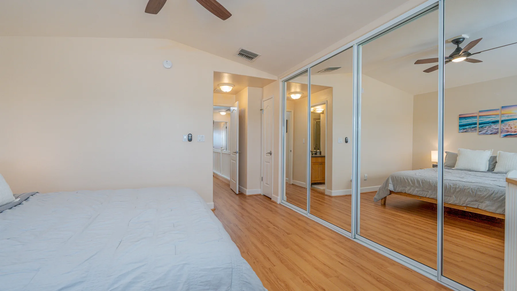 A bedroom with beds, mirrored closet doors, and wood flooring.