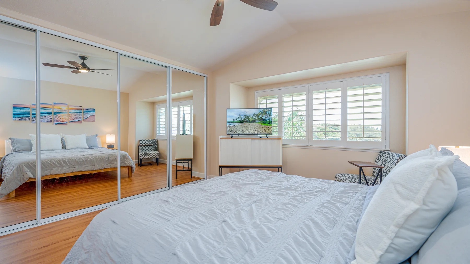 A bedroom with a bed, mirrored closet doors, and windows overlooking greenery.