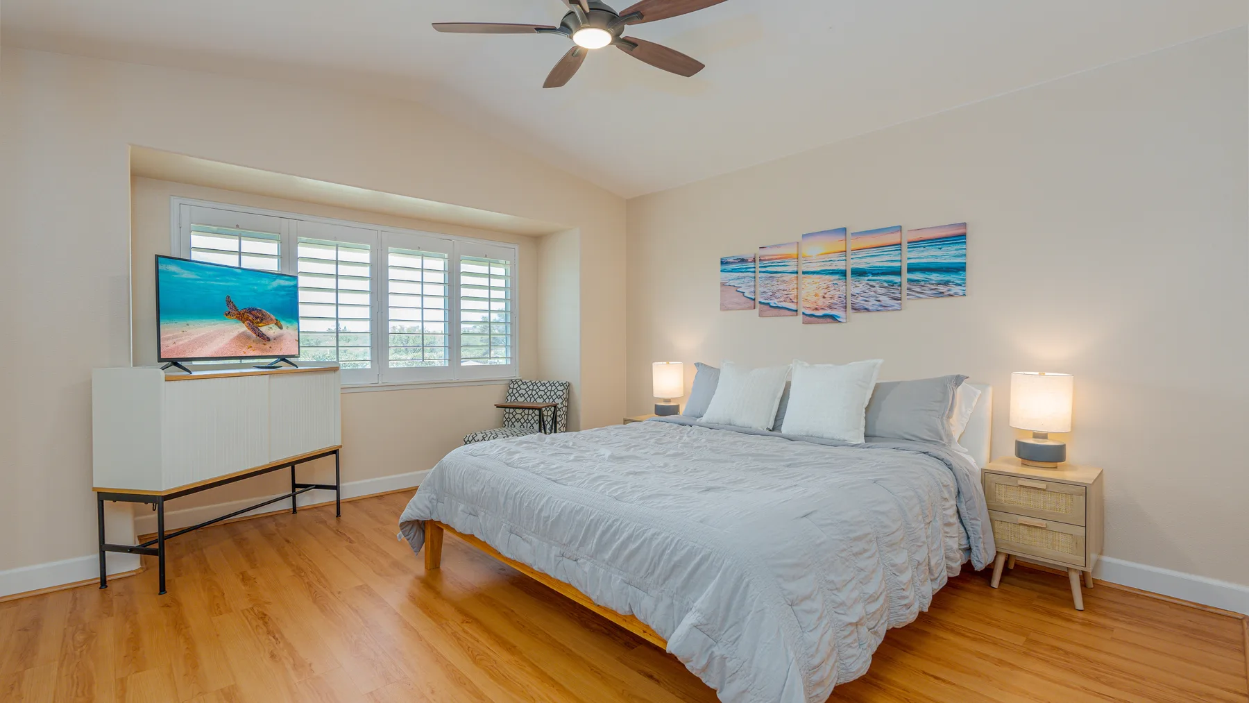 A bright bedroom features a large bed beneath colorful ocean artwork.