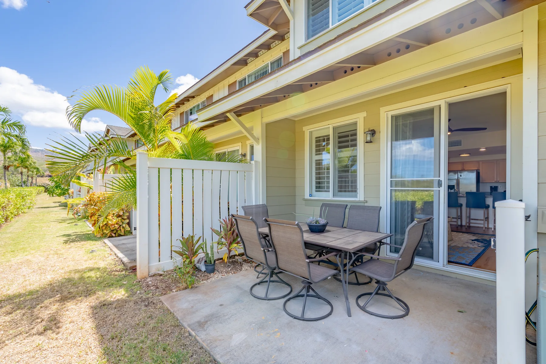 A patio with outdoor seating sits beside a sliding glass door and a fenced yard.