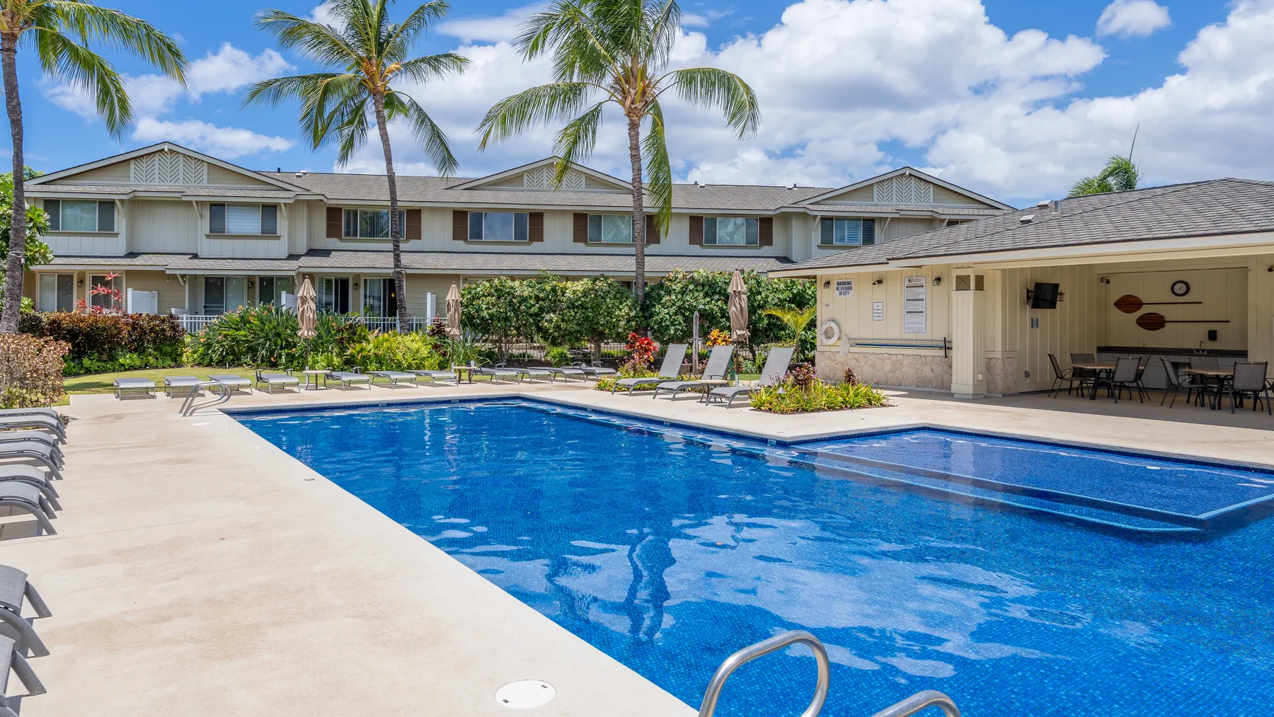 An outdoor swimming pool beside a residential building, with lounge seating around the deck.
