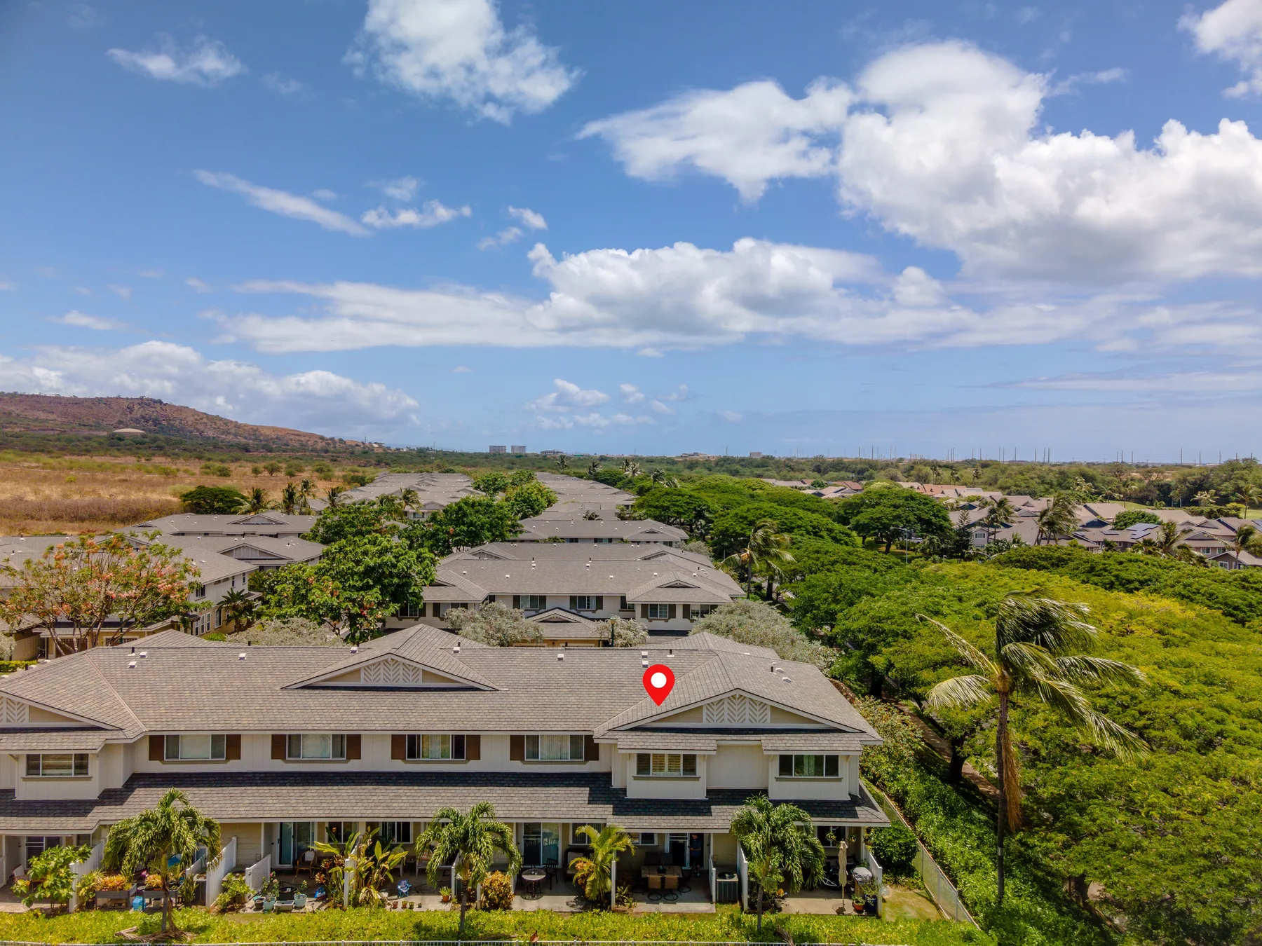 Aerial view of a low-rise residential complex surrounded by green vegetation under a partly cloudy sky.