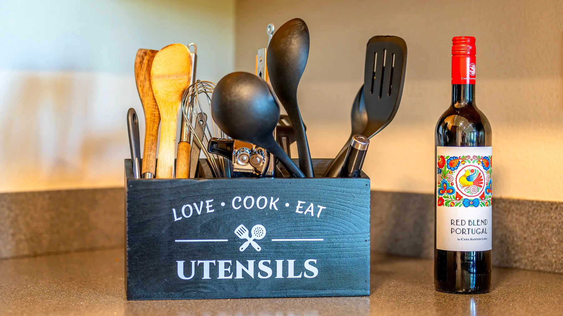Kitchen utensils stand in a countertop holder beside a bottle of wine.