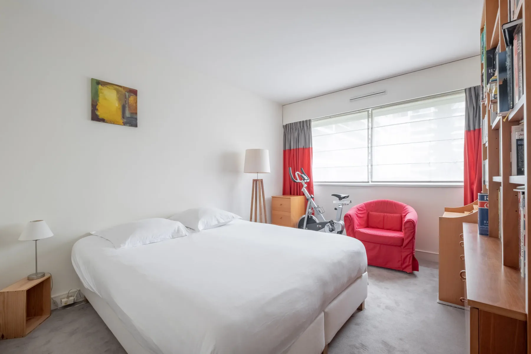 A bedroom with a large bed, a red armchair, and a wide window.