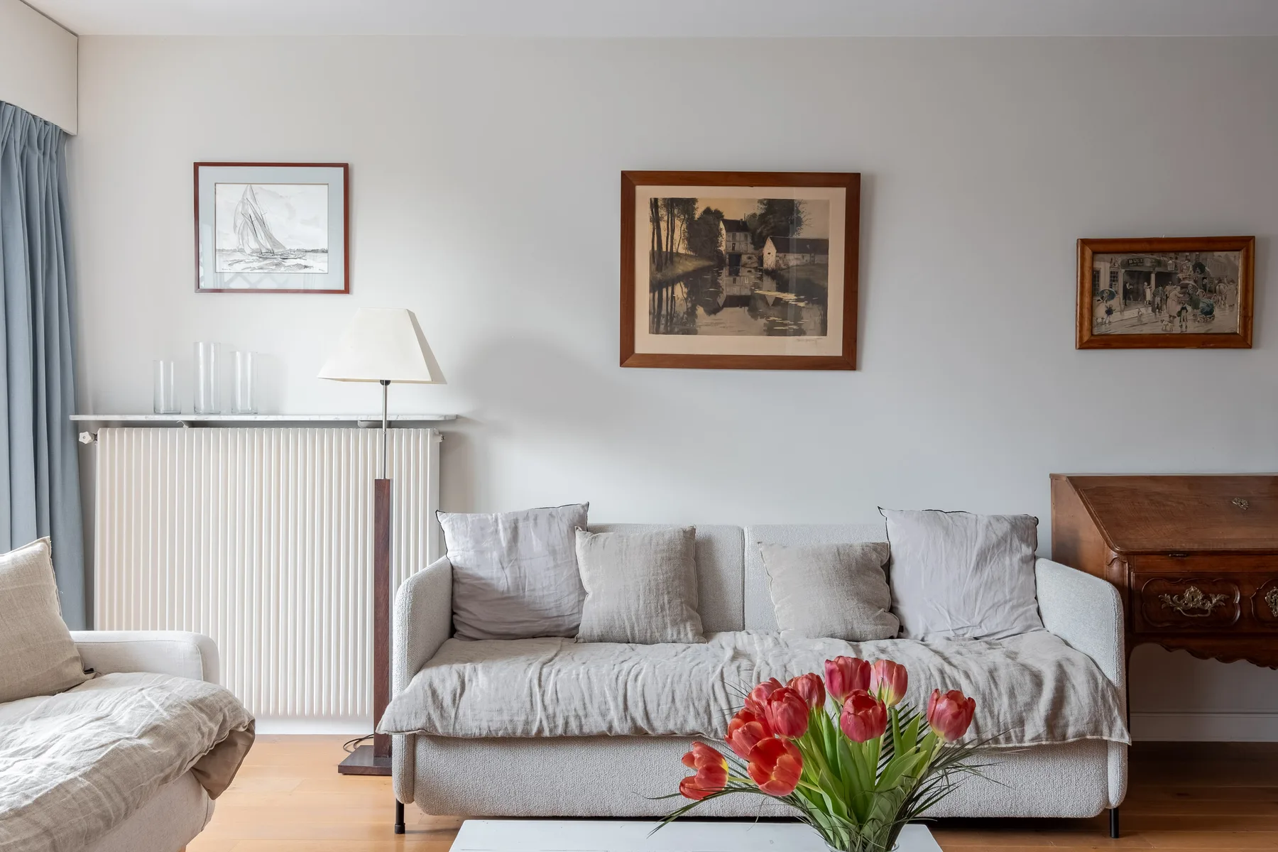 A bright living room with a sofa, framed artwork, and flowers.