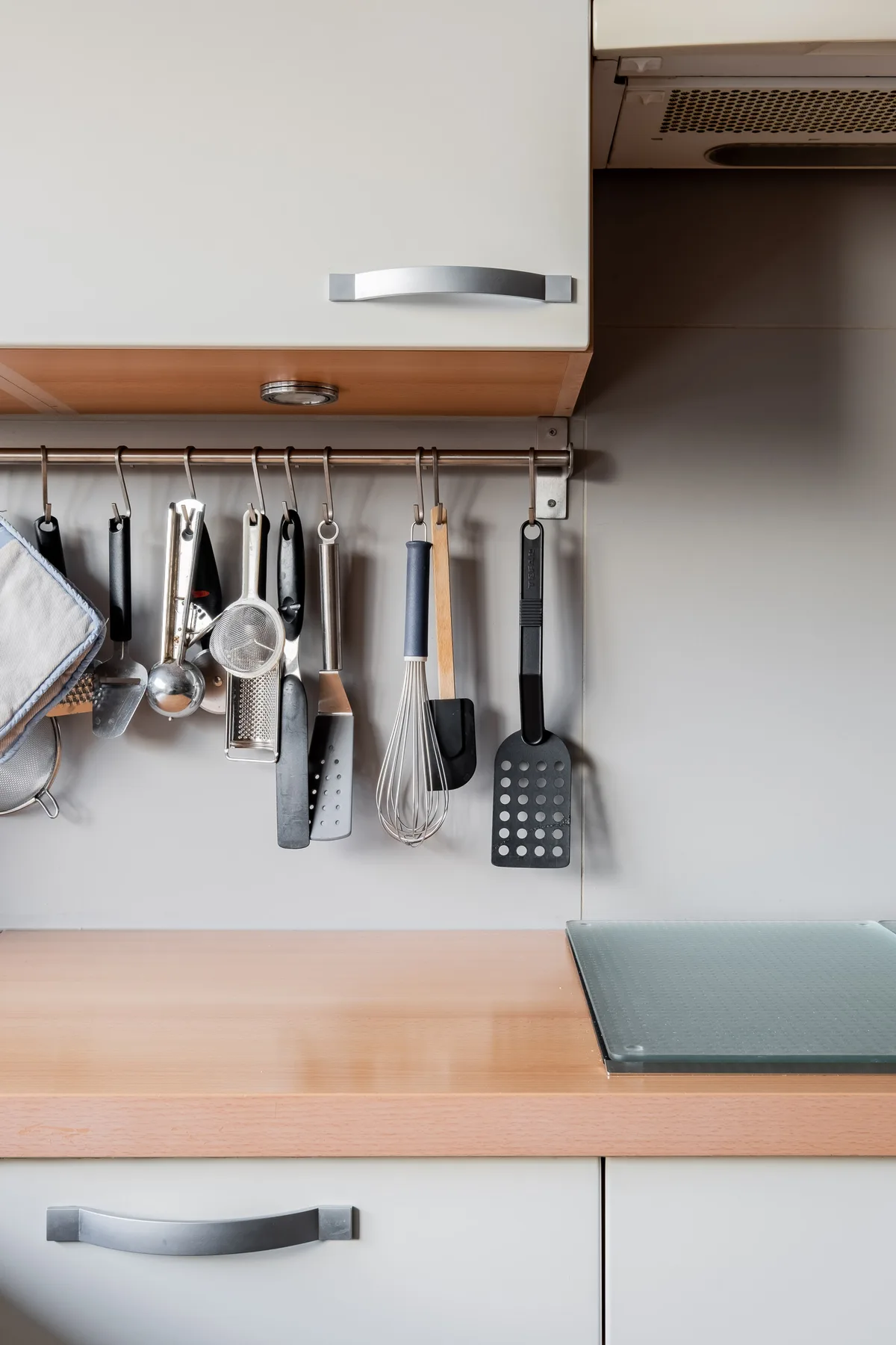 A kitchen counter sits beneath cabinets, with cooking utensils hanging on the wall.