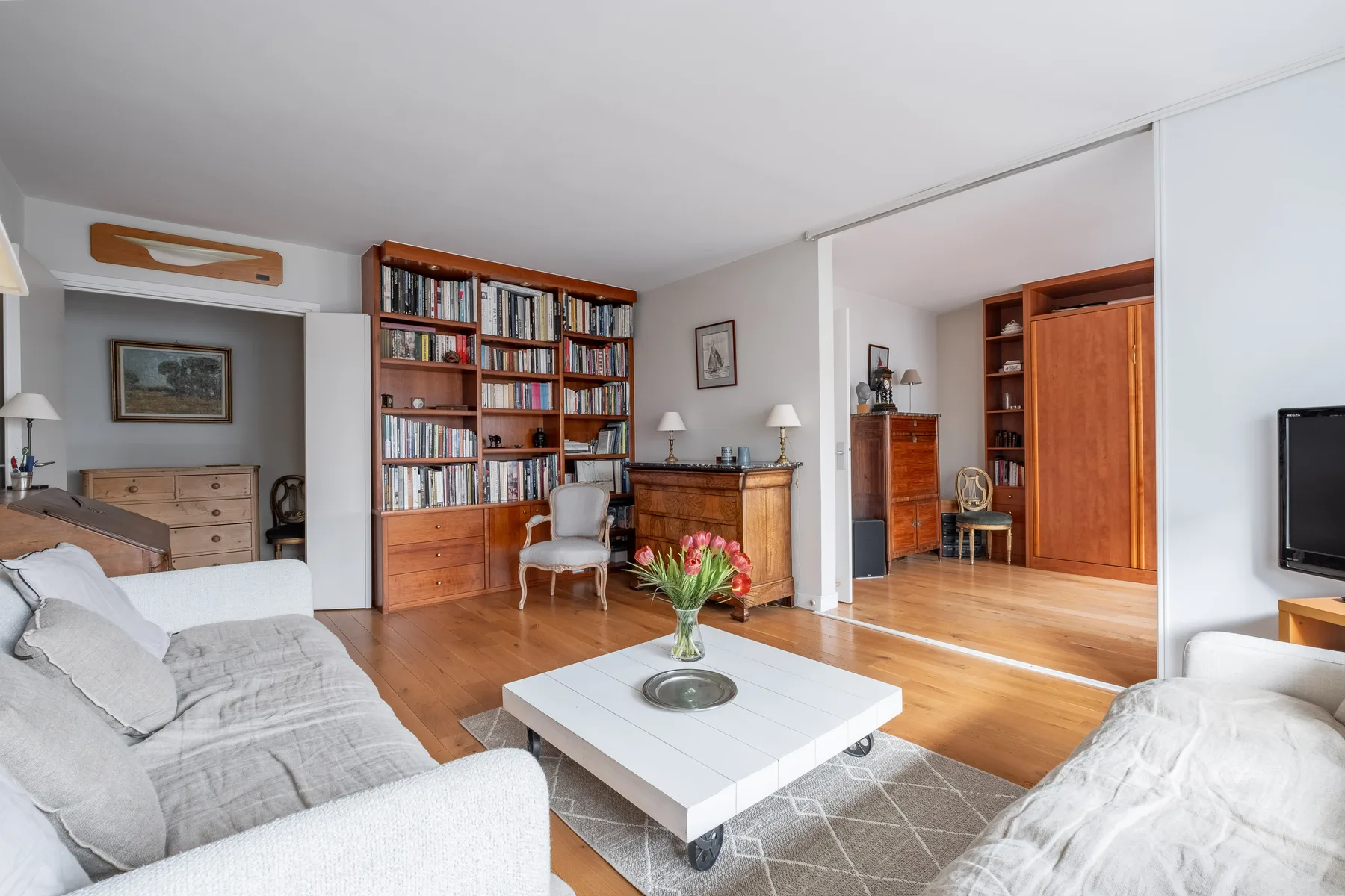 A bright living room with seating, a coffee table, and bookshelves.