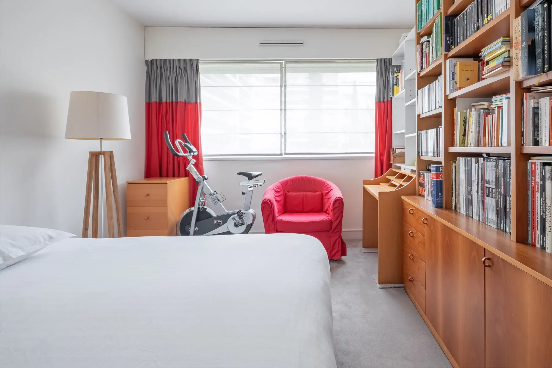 A bedroom with a bed, exercise bike, and bookshelves.
