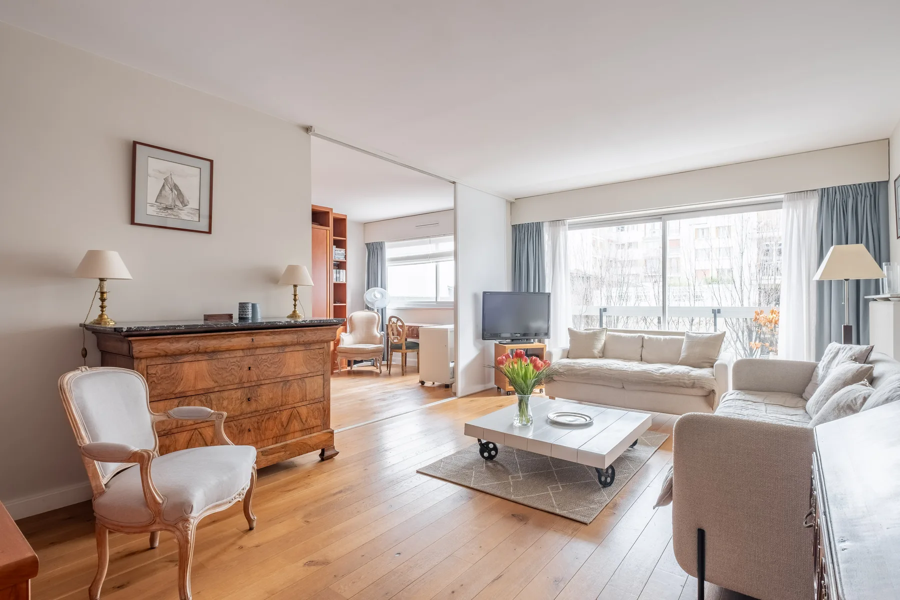A bright living room with light seating, a coffee table, and large windows.