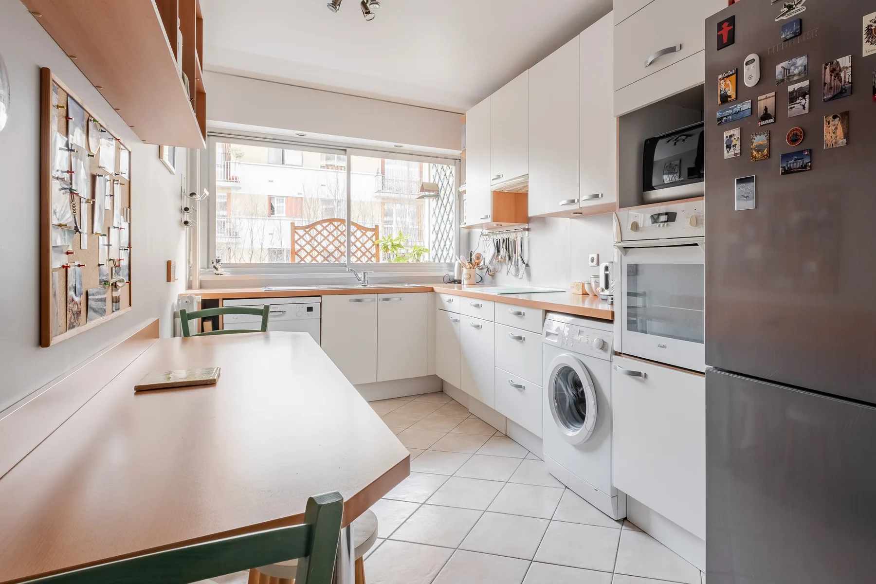 A bright kitchen with white cabinets, a dining table, and a large window.