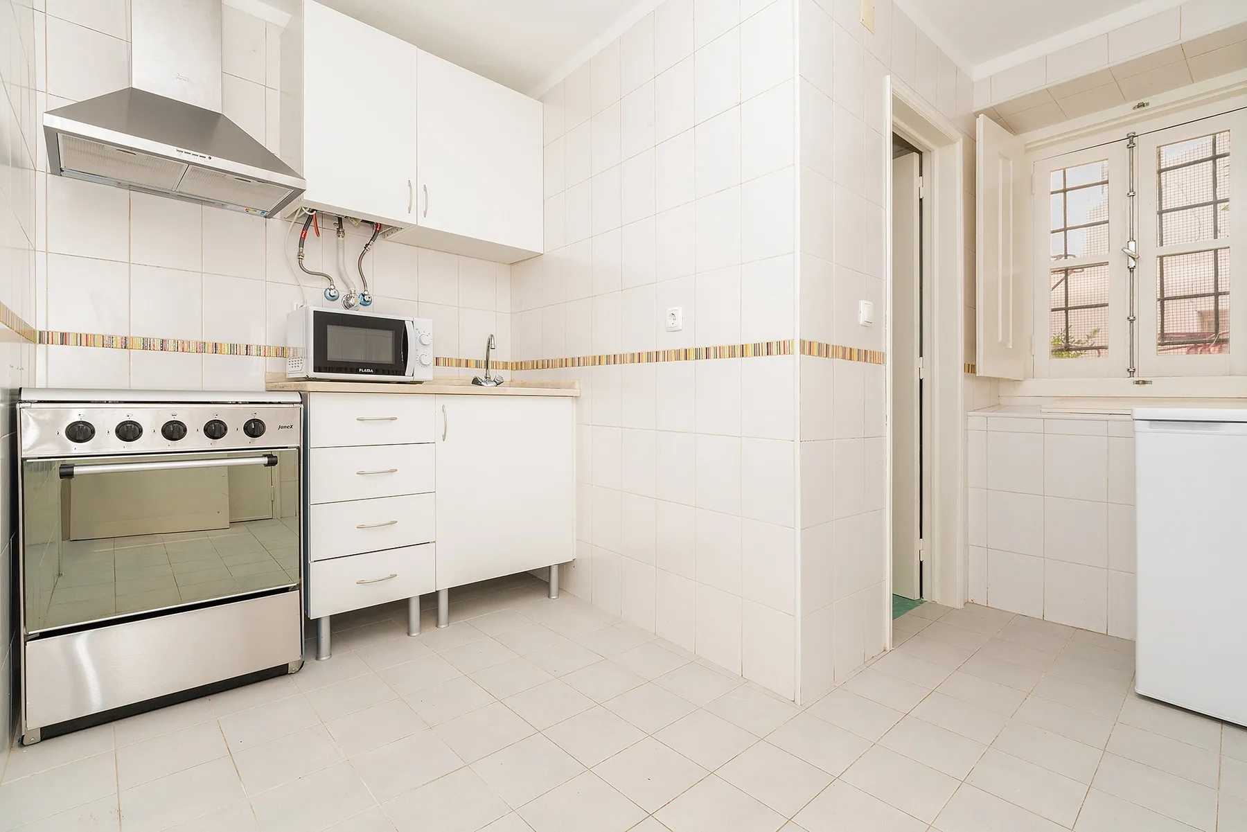 A bright tiled kitchen with white cabinets and a built-in oven.