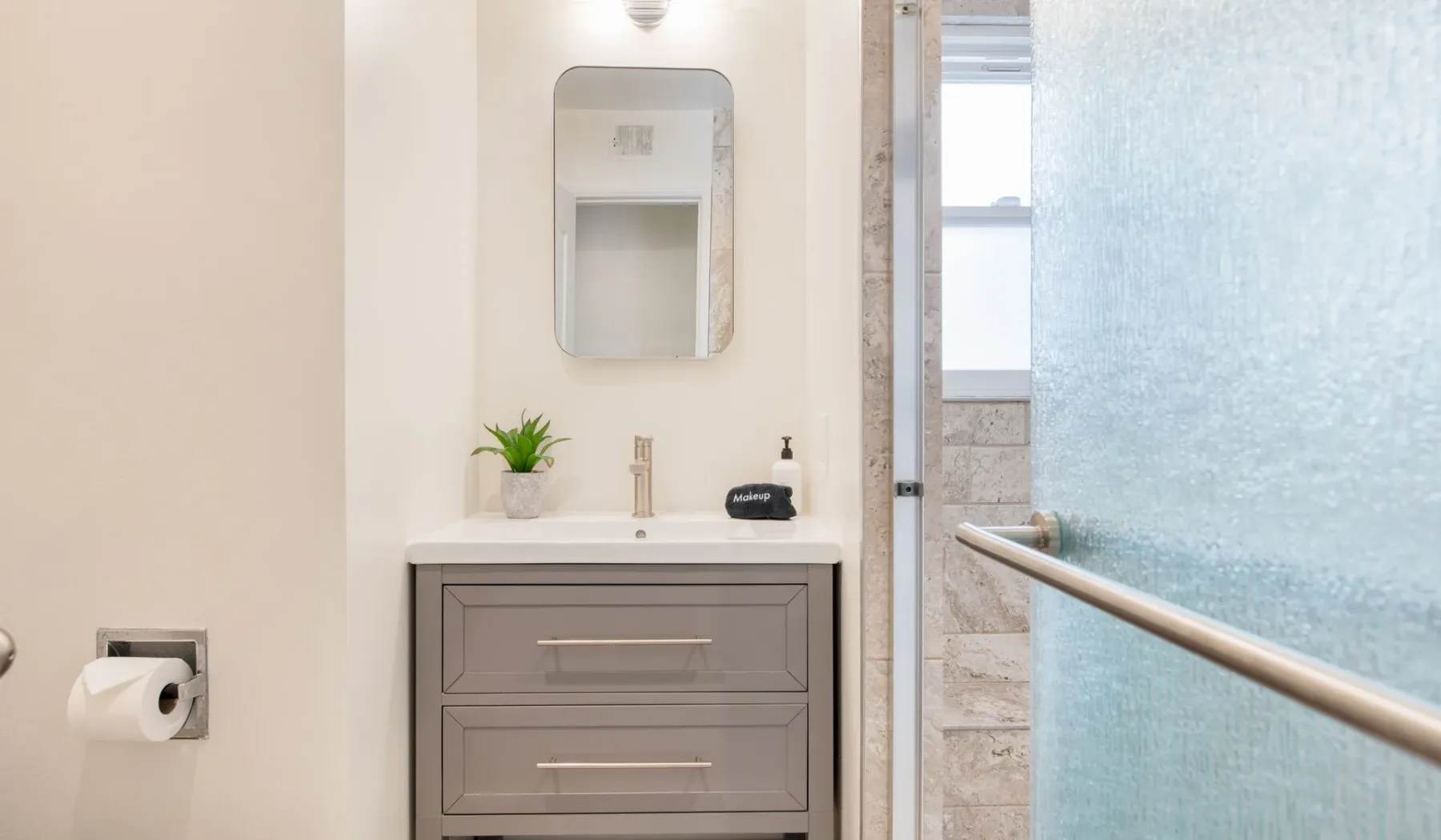 Un tocador de baño con espejo junto a una ducha de vidrio.