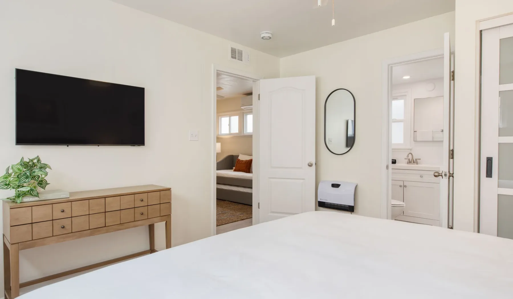 Un dormitorio luminoso con cama, televisor en la pared y puertas a habitaciones contiguas.