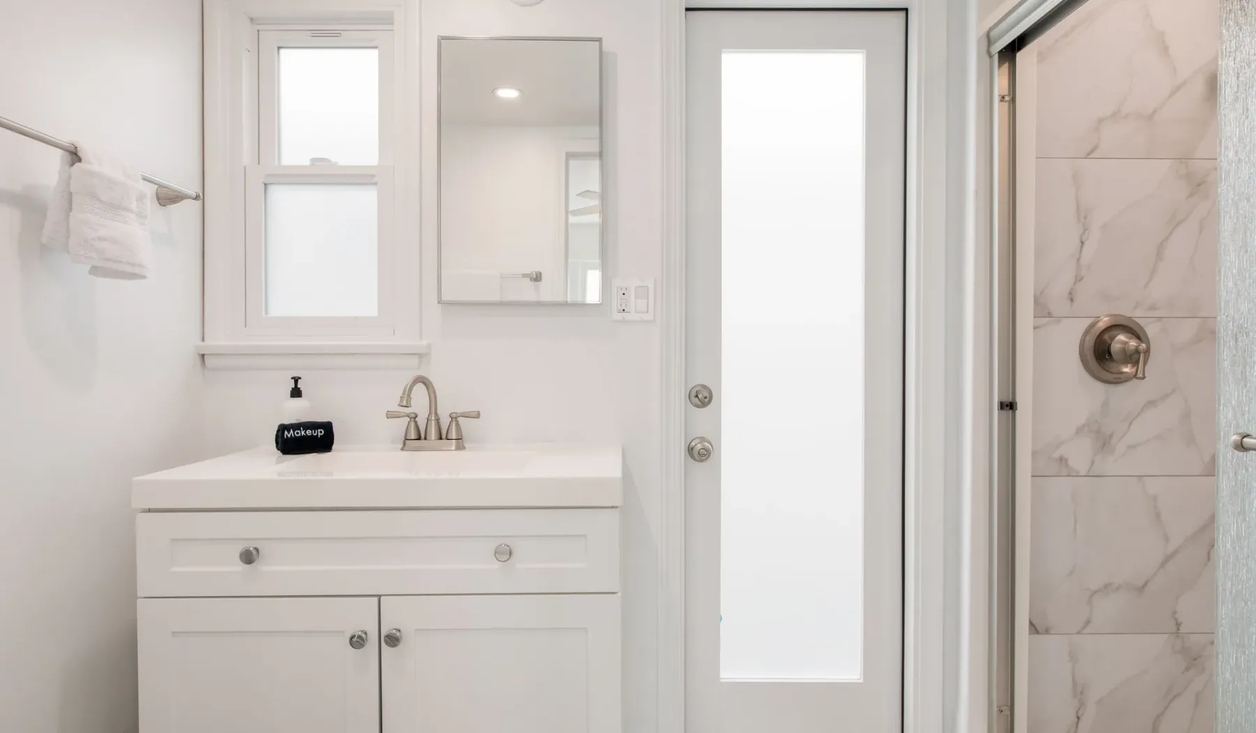 Un tocador de baño luminoso con espejo junto a una ducha de vidrio.