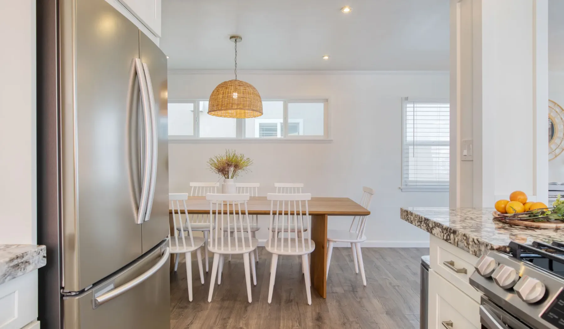 Comedor con mesa de madera, asientos blancos y una lámpara colgante de fibras tejidas.