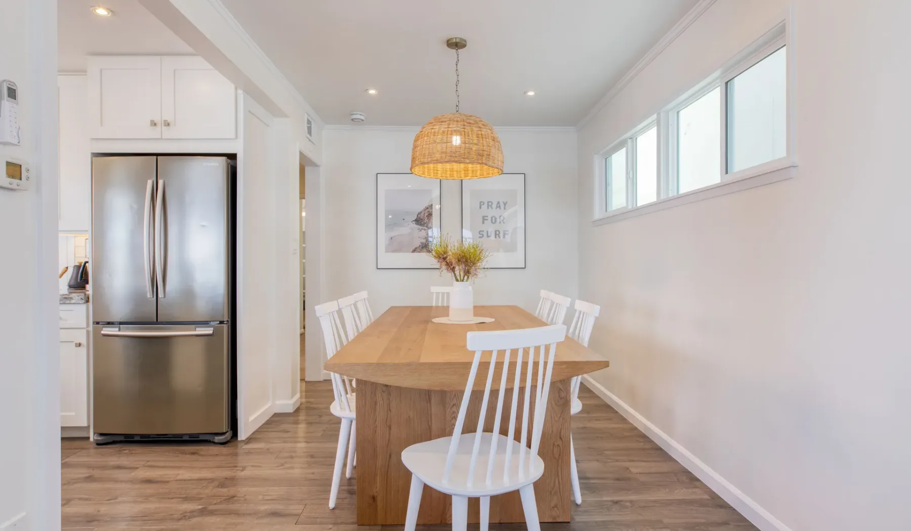 Un comedor luminoso tiene una mesa de madera bajo una lámpara colgante tejida.