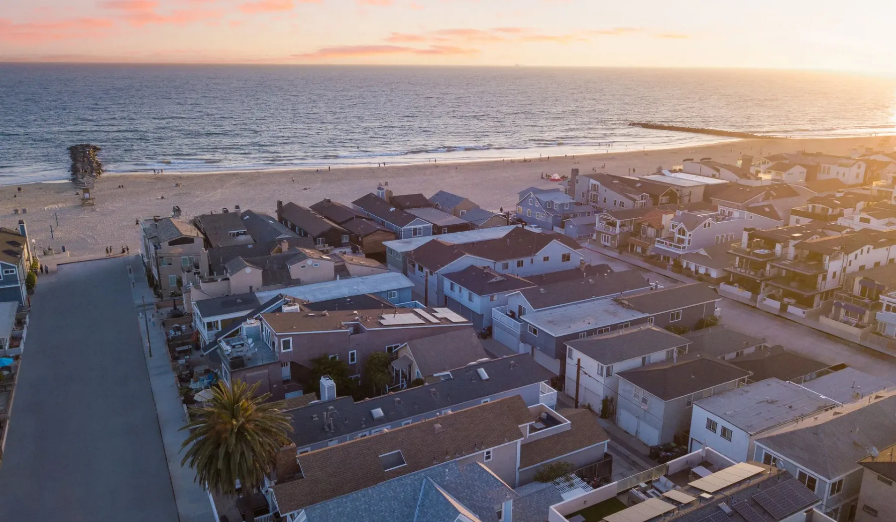 Vista aérea de casas costeras junto a una playa de arena al atardecer.