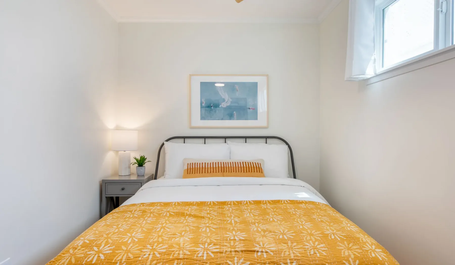 Un dormitorio con una cama cubierta por una manta amarilla estampada y un cuadro encima.