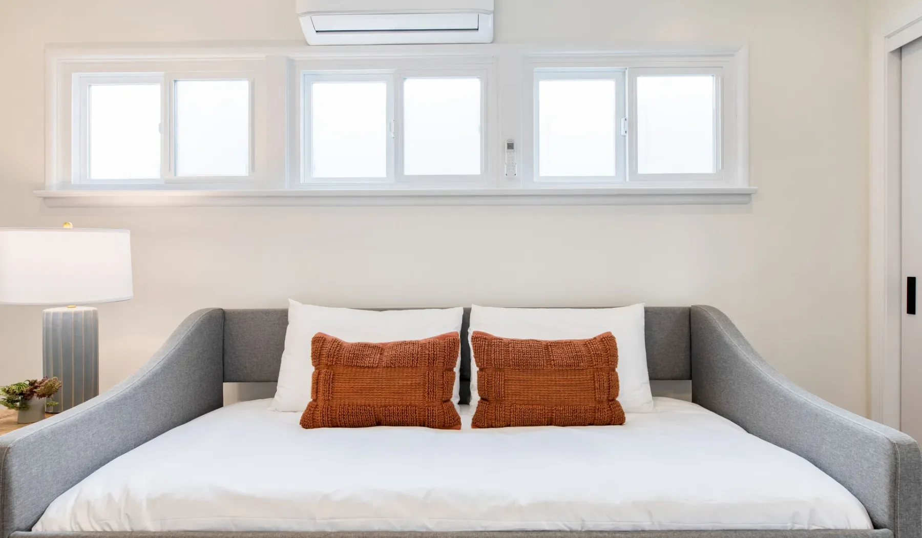 Un dormitorio con una cama bien hecha y dos cojines color óxido.