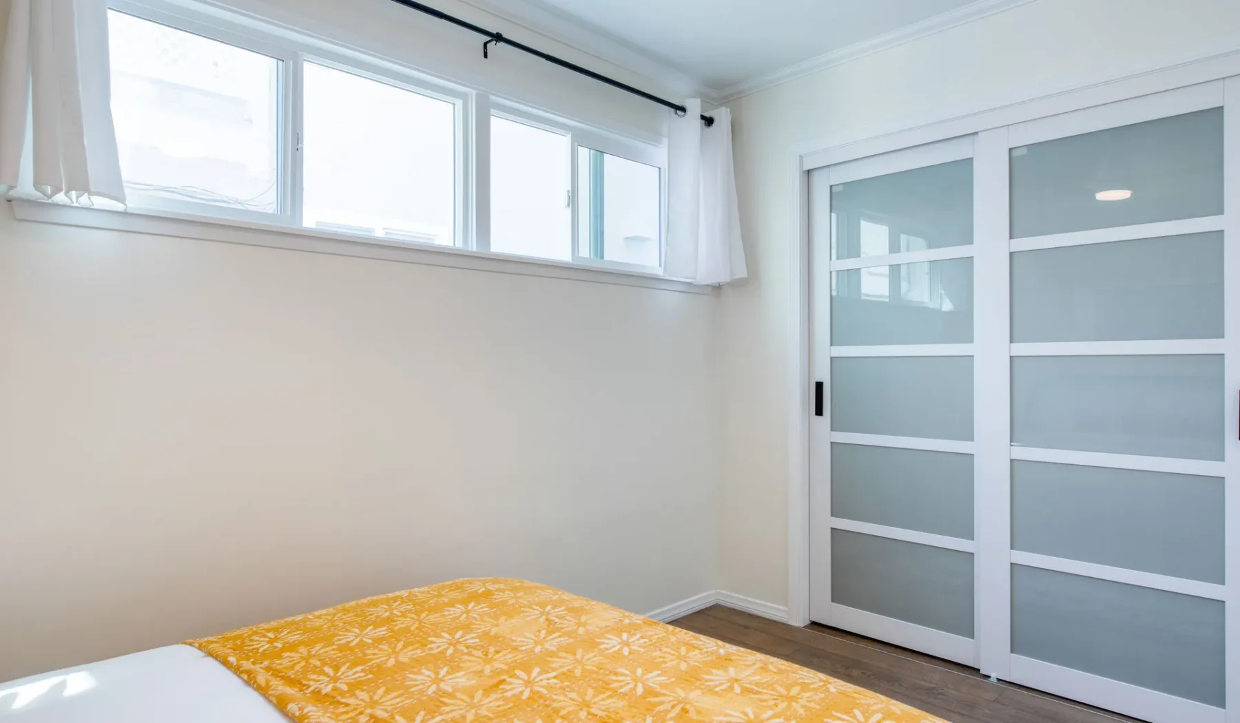 Dormitorio con una cama cubierta con una manta amarilla estampada junto a una puerta corrediza.