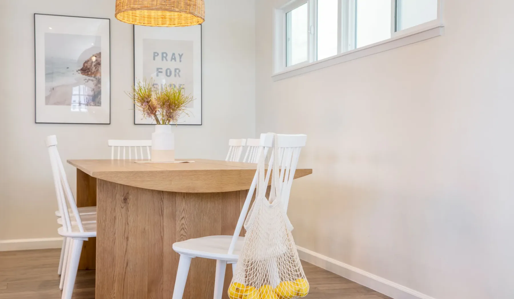 Un comedor luminoso con una mesa de madera, sillas blancas y cuadros en la pared.