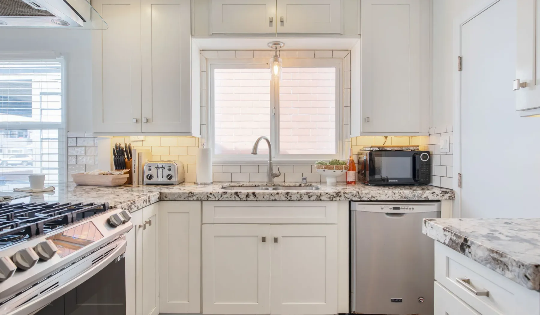 Una cocina luminosa con gabinetes blancos, un fregadero central y electrodomésticos de acero inoxidable.
