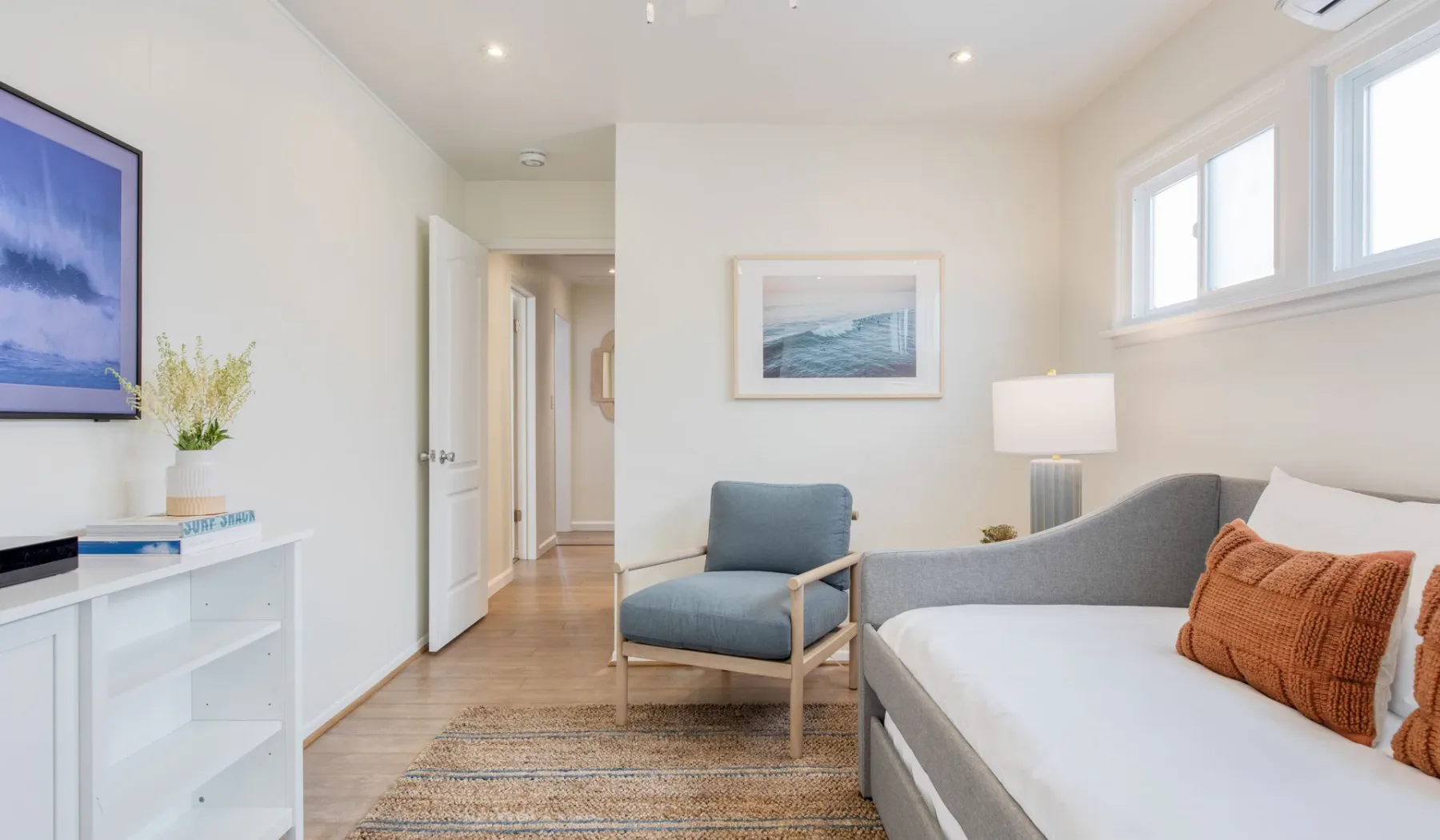 Un dormitorio luminoso con cama, asientos y cuadros de temática costera.