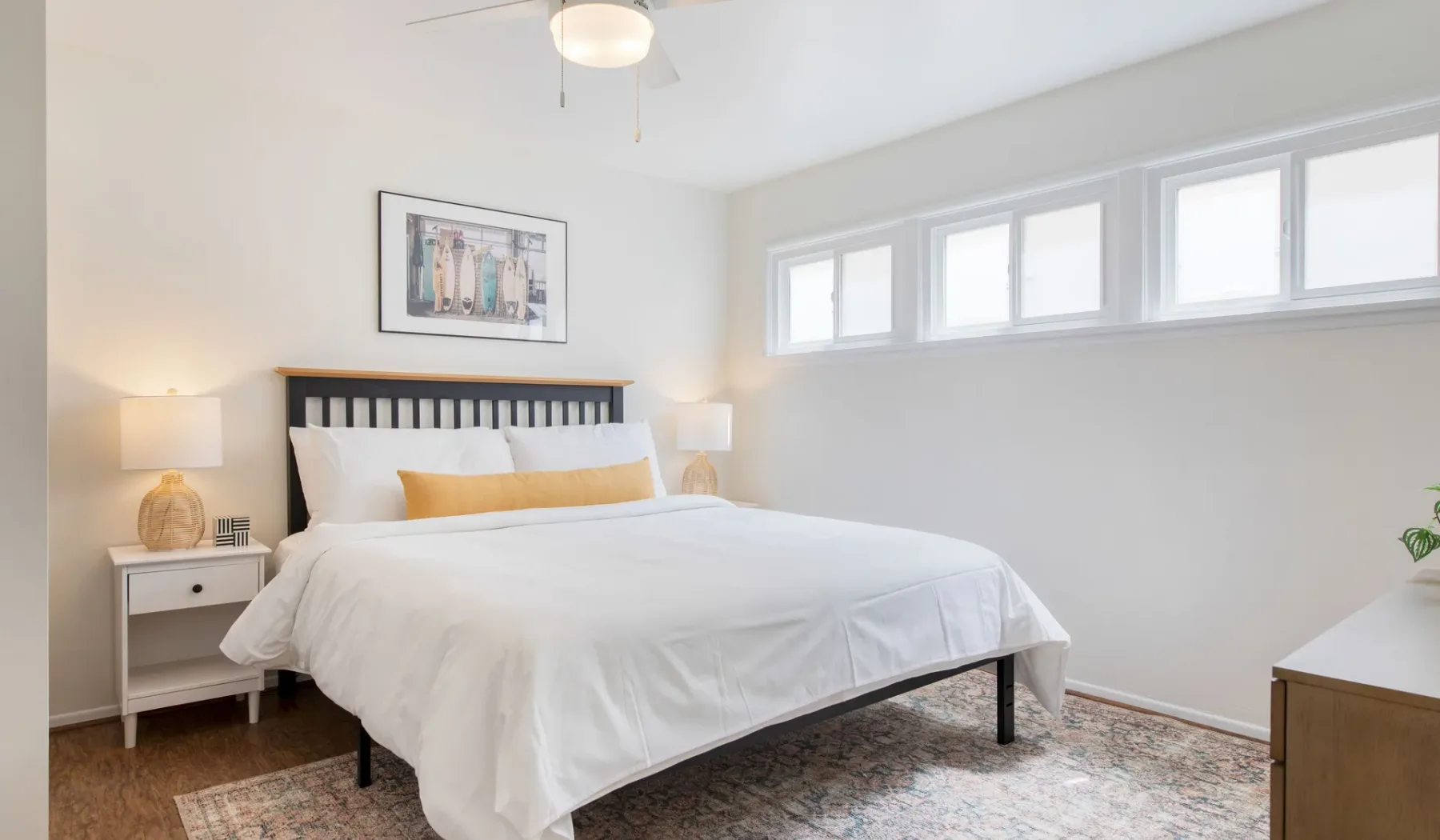 Un dormitorio luminoso con una cama bien tendida bajo una fila de ventanas.