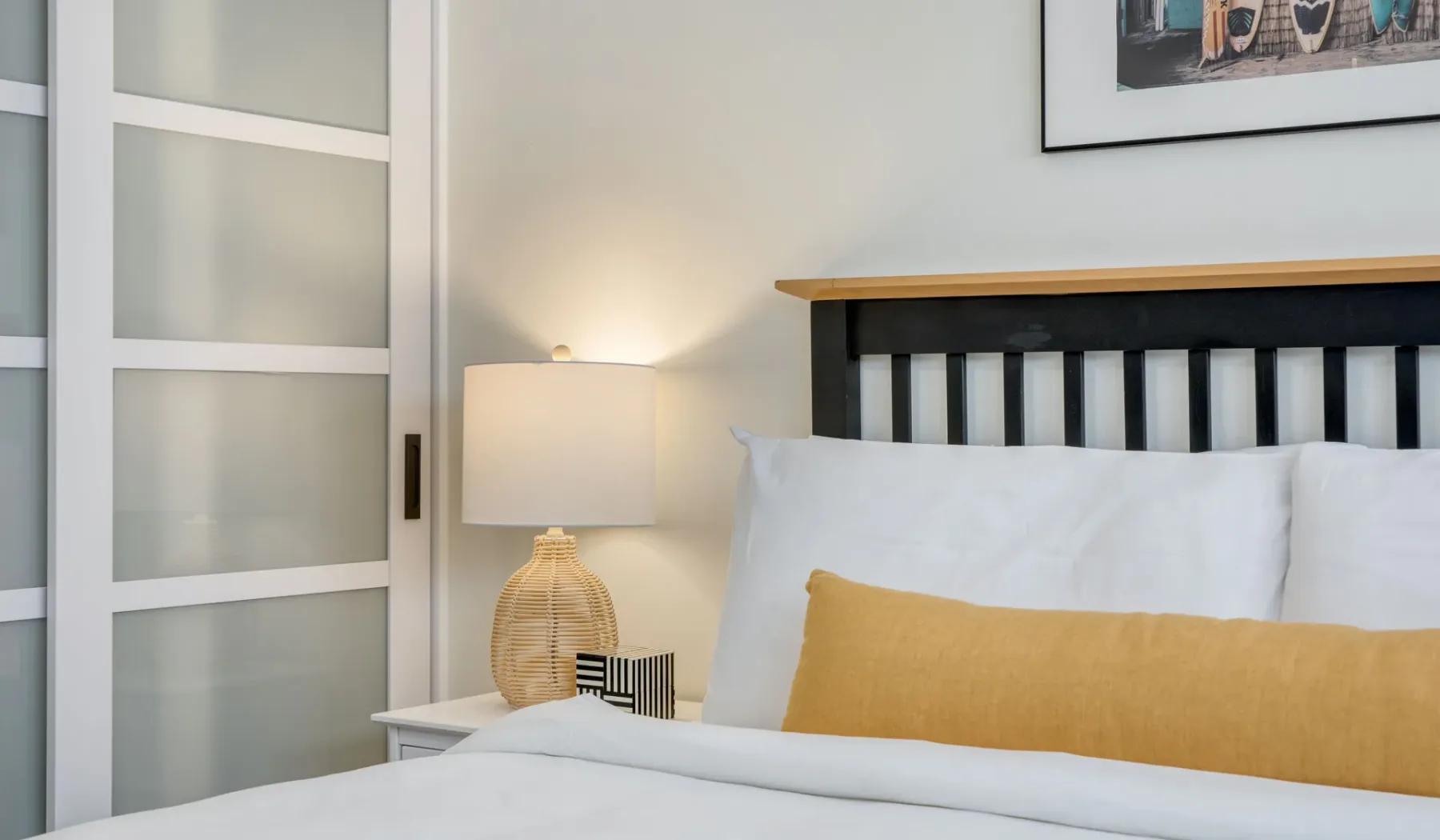 Un dormitorio con ropa de cama blanca y un cojín decorativo color mostaza.
