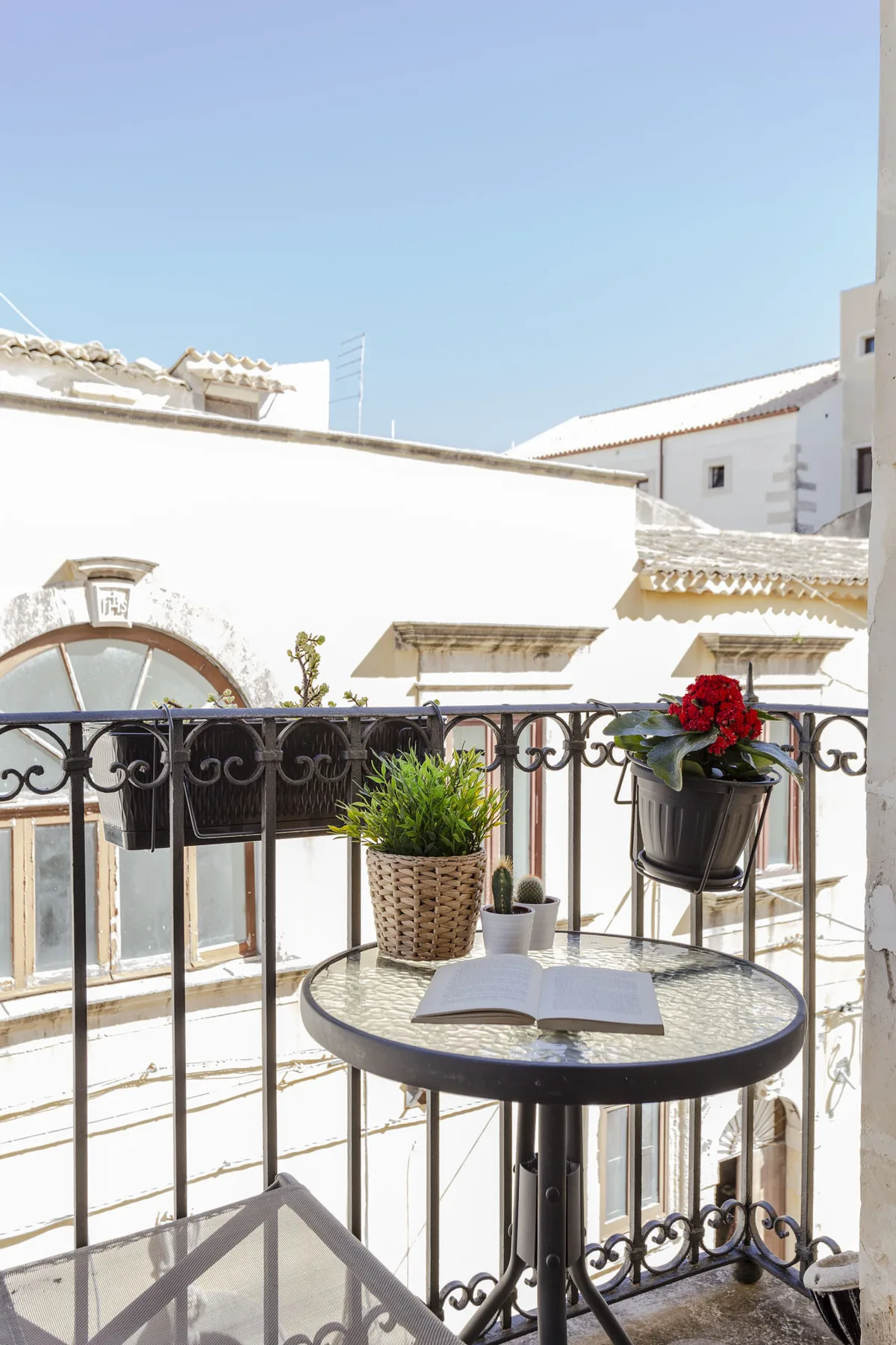 A small balcony with a round table, potted plants, and views of nearby buildings.