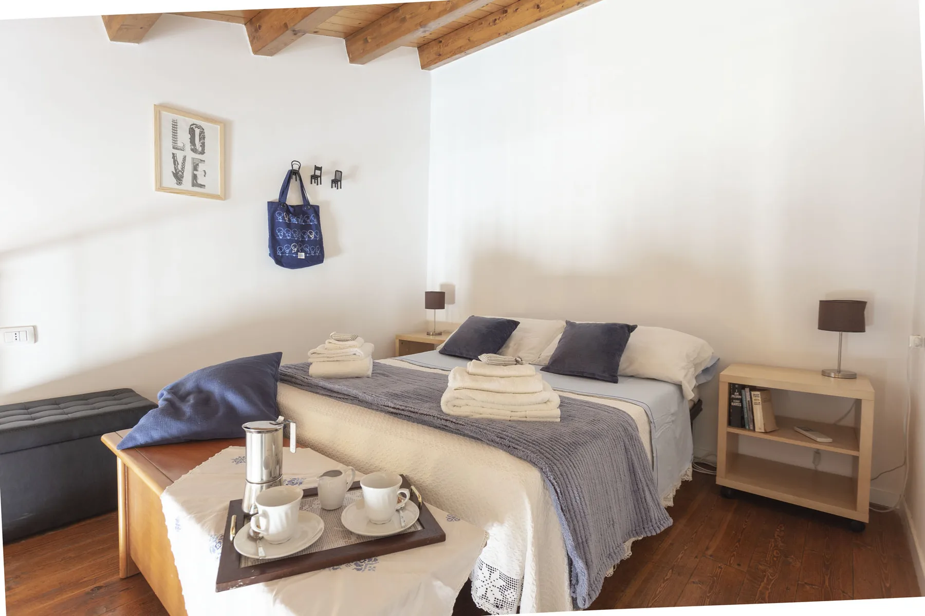 A bedroom with a bed dressed in gray linens and folded towels.