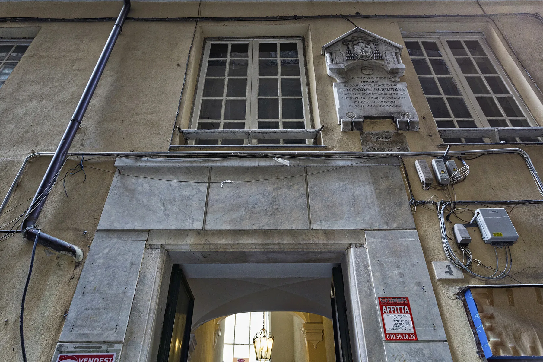 Entrada exterior de un edificio enmarcada por piedra, con ventanas y una placa encima.