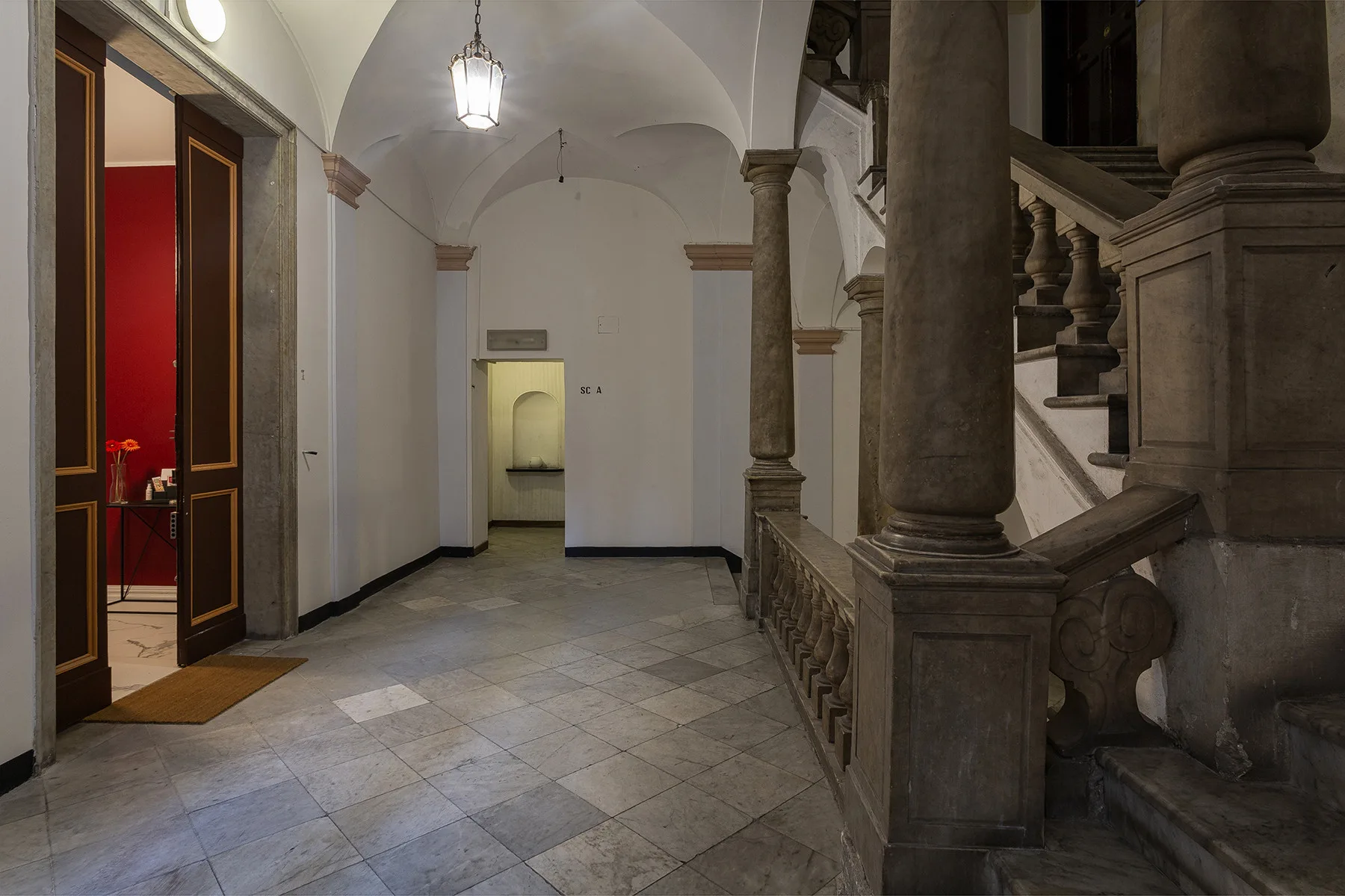 Un pasillo interior de baldosas con una puerta abierta y una escalera de piedra.